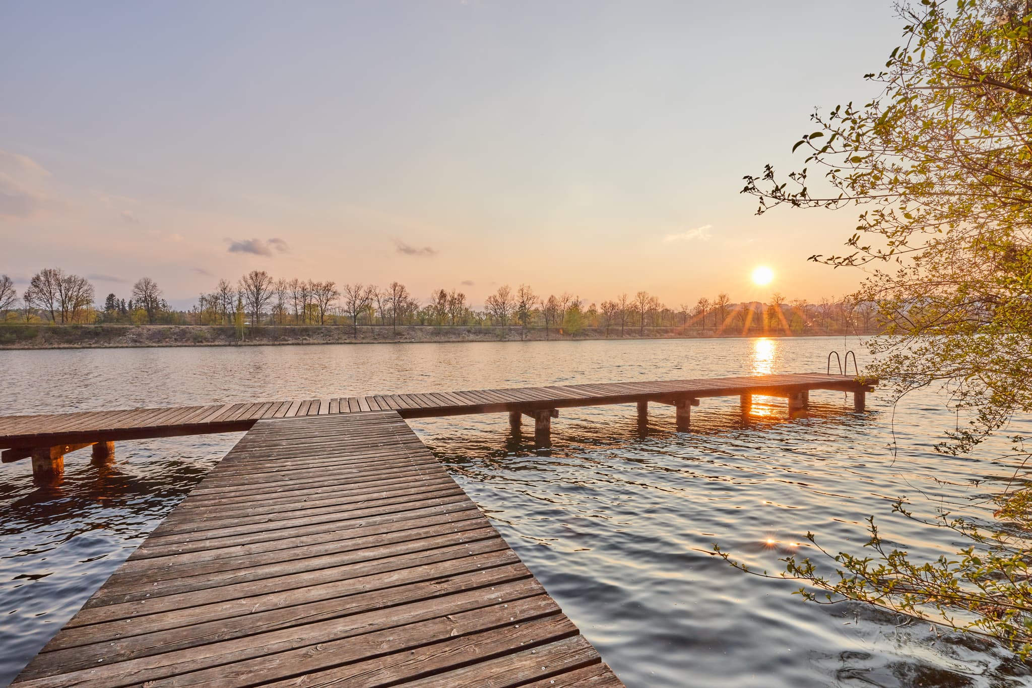 Idyllischer Sonnenuntergang am Marktler Badesee in Oberbayern, Inn-Salzach Region, Deutschland. Holzsteg am See bei Sonnenuntergang. Genießen Sie die Natur.