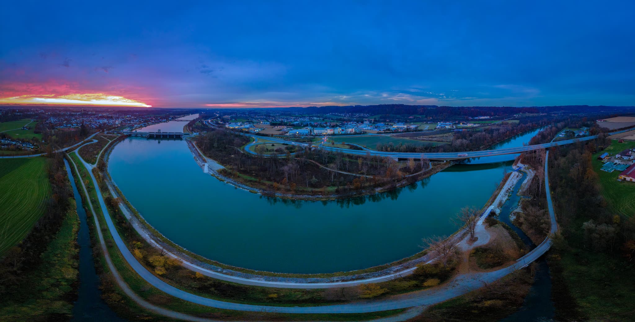 Sonnenuntergang über Neuötting, Landkreis Altötting, Oberbayern. Panorama des Inns mit Wehr und Stadtansicht bei Dämmerung.