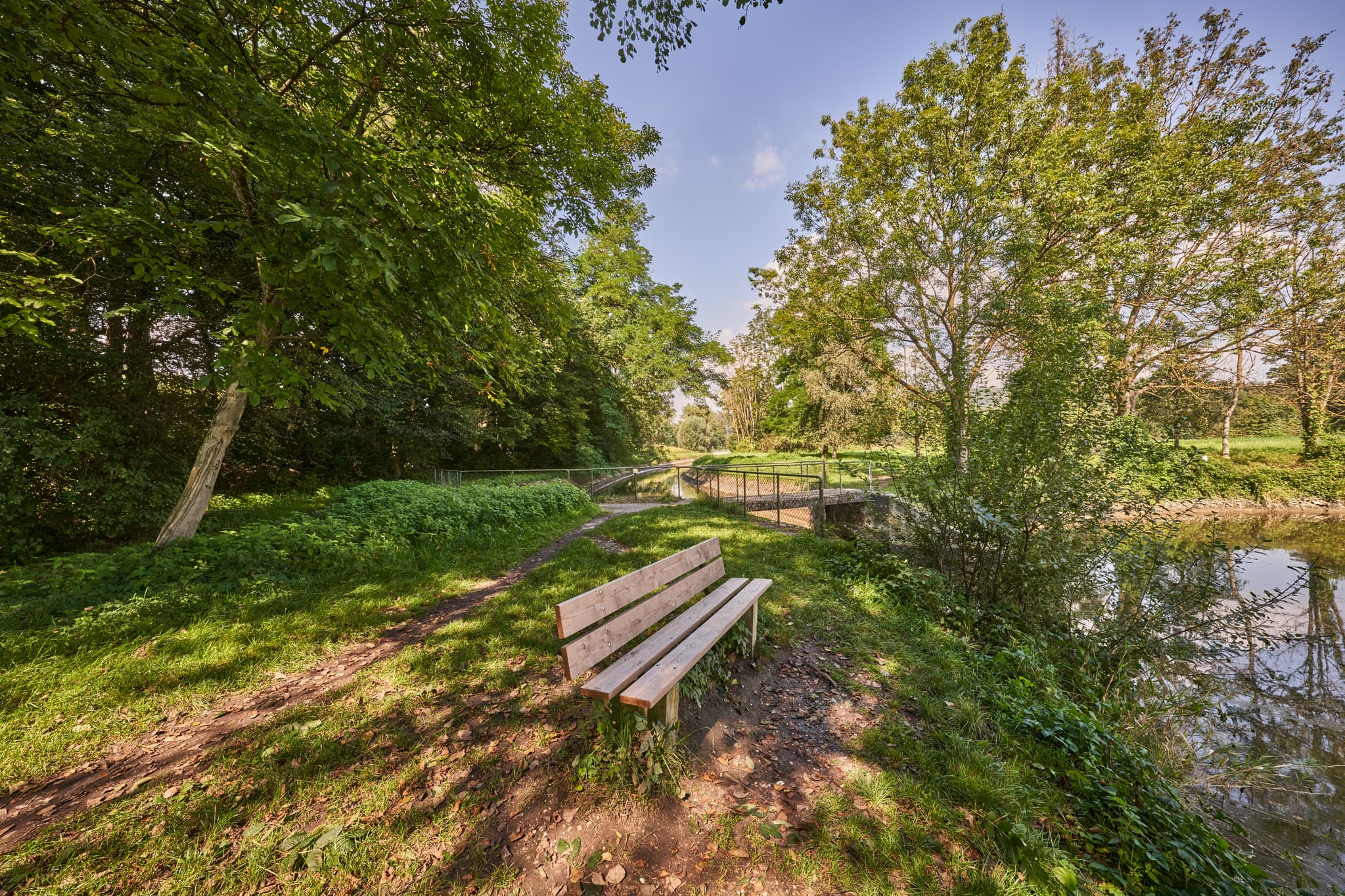 Idyllische Landschaft am Stauweiher in Winhöring, Altötting, Oberbayern. Ruhiger Weg mit Holzbank am Gewässer. Teil der Inn-Salzach Region in Deutschland.