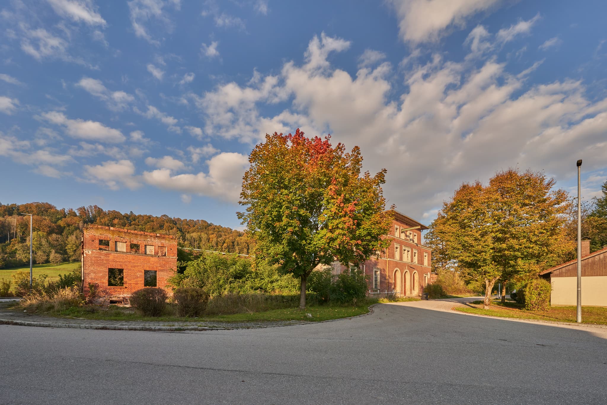 Eisenfelden in Winhöring, Altötting, Oberbayern, Inn-Salzach, Deutschland. Bahnhof Neuötting mit alten Gebäuden und Herbstbäumen unter blauem Himmel.