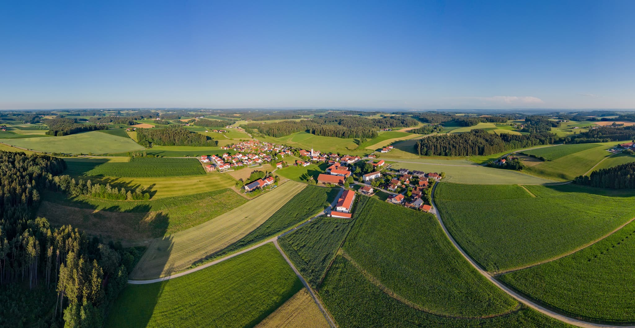 Blick auf Erlbach im Landkreis Altötting, Oberbayern, Deutschland. Agrarflächen und Wälder bei klarem Himmel.