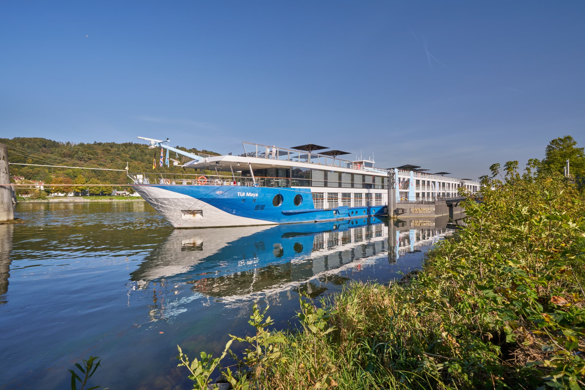 Flusskreuzfahrtschiff am Donau Hafen in Vilshofen, Landkreis Passau, Niederbayern, Deutschland. Zeigt das Schiff und die Donau-Wald-Landschaft bei Sonnenschein.