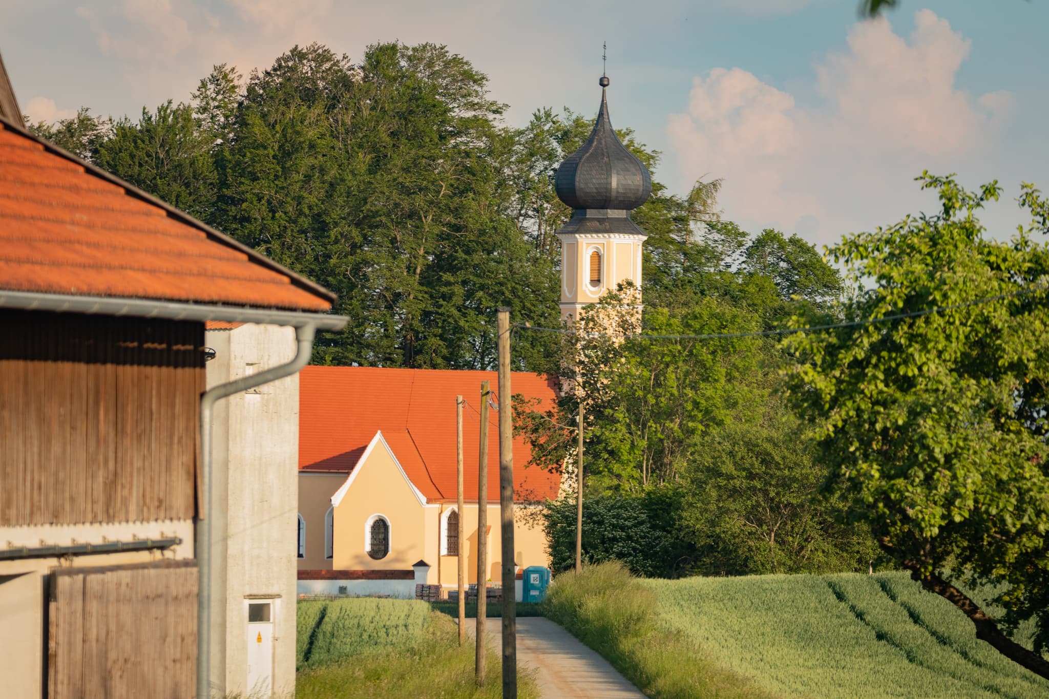Kirche Sankt Sebastian in Leonberg, Marktl, Landkreis Altötting, Oberbayern. Region Inn-Salzach, umgeben von Feldern und Bäumen.