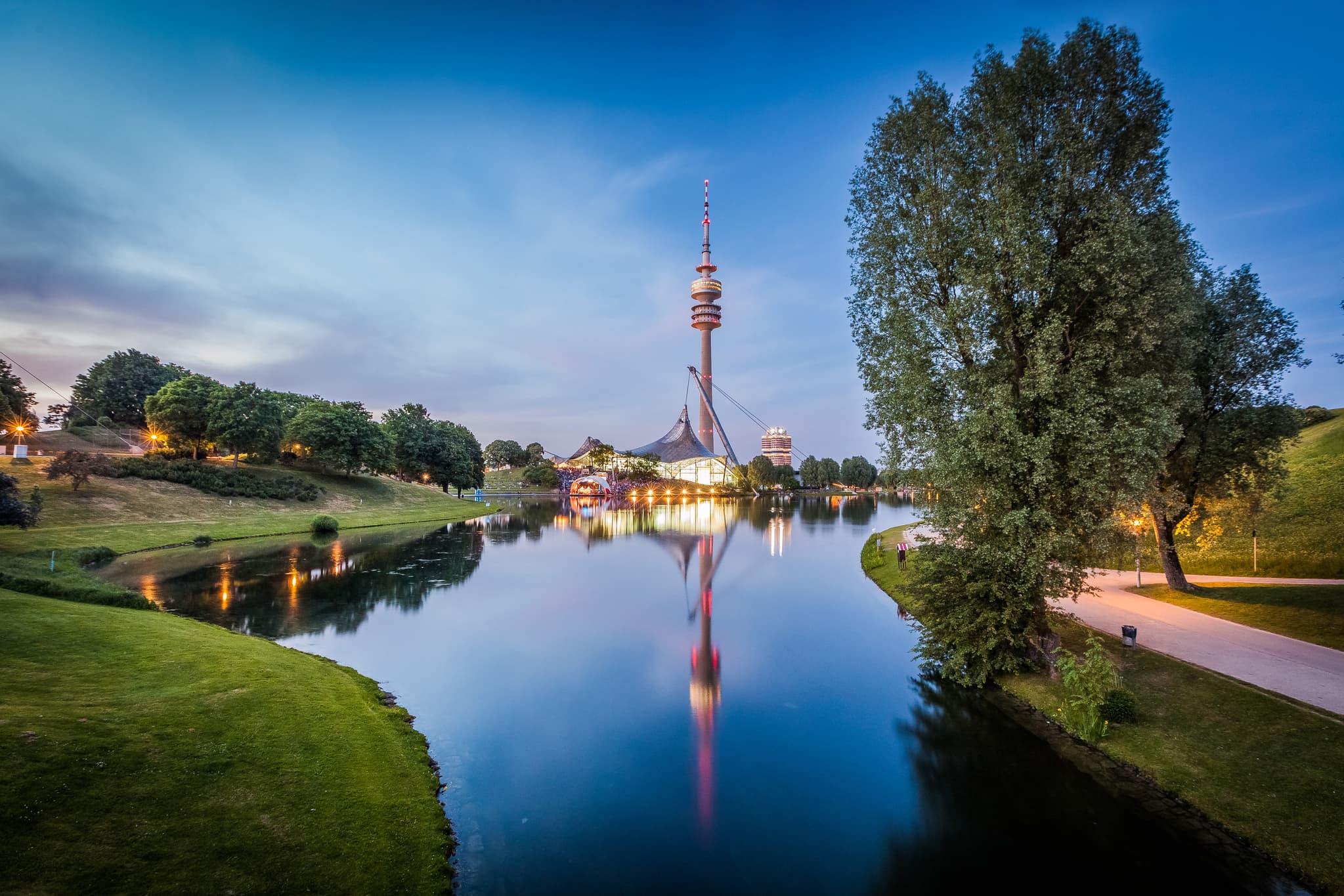 Olympiapark in München ist ein Wahrzeichen der Metropolregion München in Oberbayern, Deutschland. Das Bild zeigt die Anlage mit dem Olympiaturm und einem See.