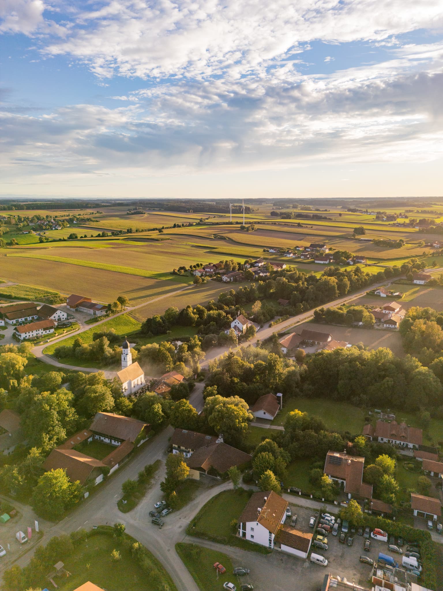 Ortsansicht Dirnaich, Gangkofen, Rottal-Inn, Niederbayern. Ein Windpark prägt die Landschaft im Holzland. Weite Felder unter Sonnenuntergang in Deutschland.