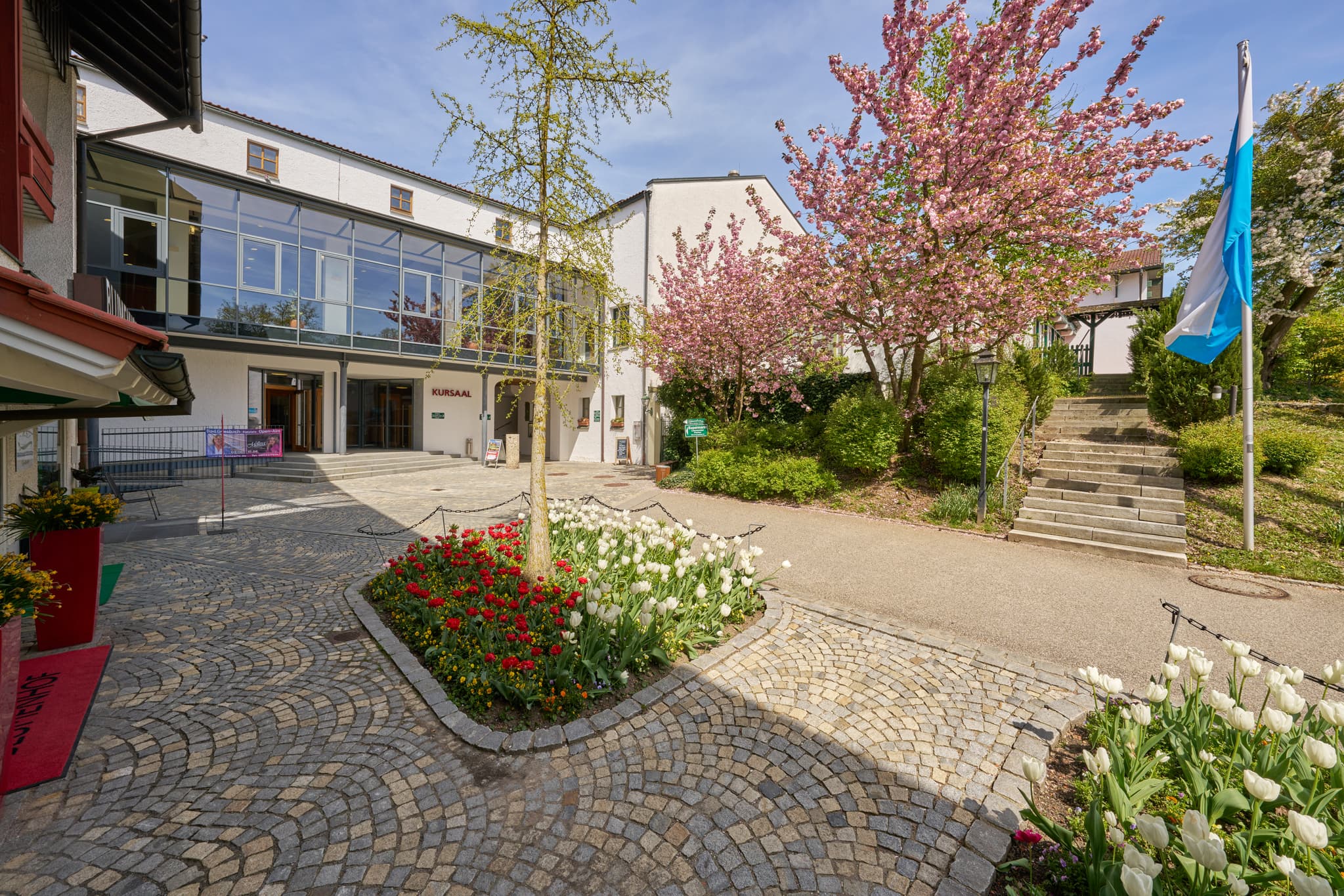 Frühlingsansicht des Kursaals in Bad Griesbach, Landkreis Passau, Niederbayern. Zeigt blühende Bäume, Blumen und den Vorplatz im Rottal, Deutschland.