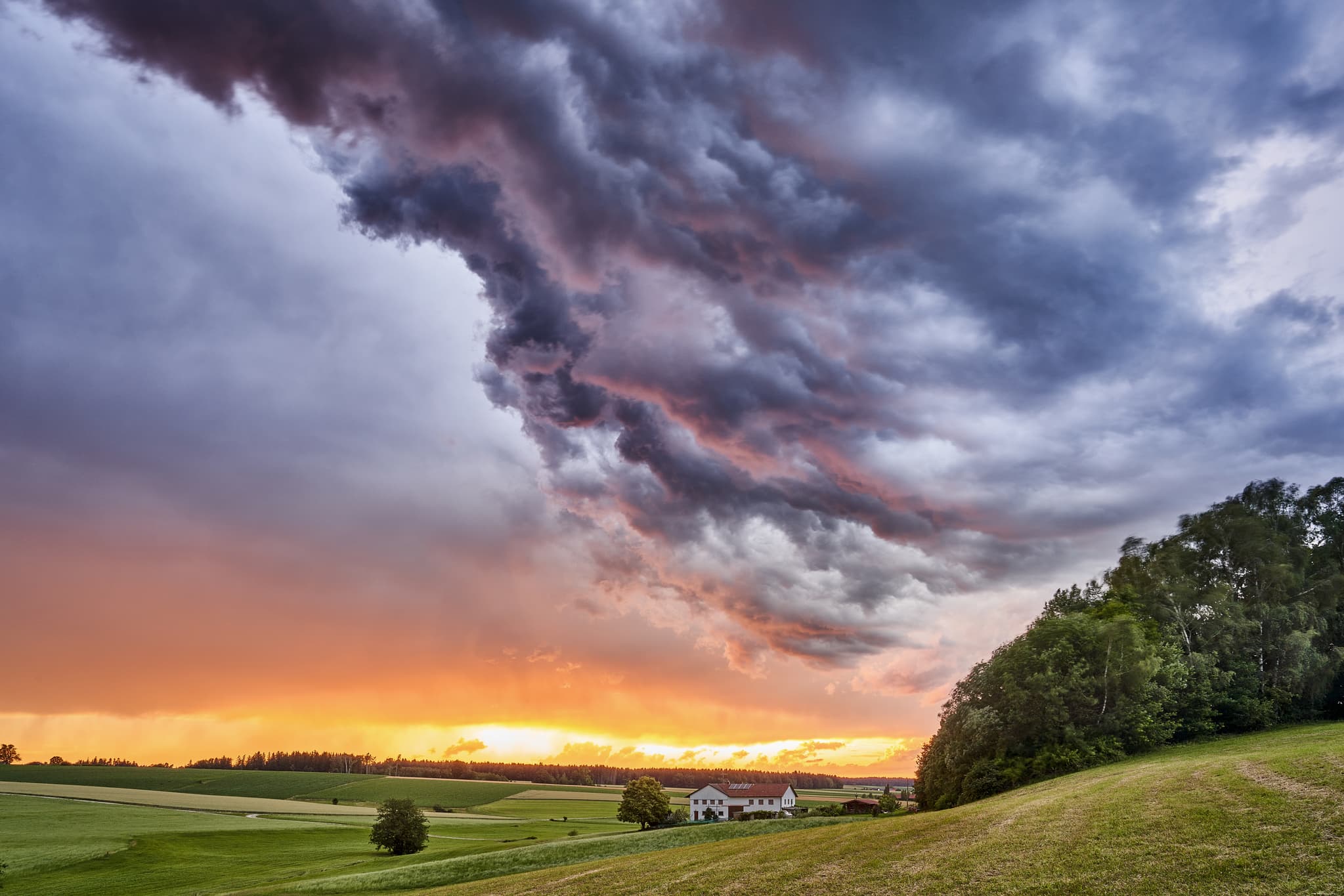 Bild zeigt eine ländliche Landschaft in Arbing, Gemeinde Reischach, Landkreis Altötting mit einem Anwesen bei Sonnenuntergang und dramatischen Wolkenformationen