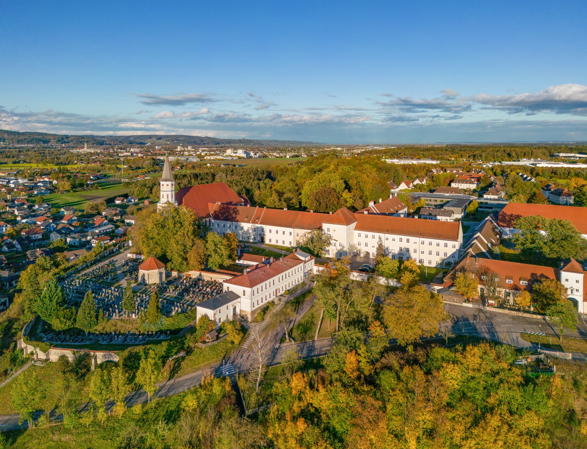 Luftbild von Schloss Ranshofen in Ranshofen, Braunau am Inn, Oberösterreich, Österreich. Gebäudeensemble, Kirche, Friedhof und Herbstlandschaft im Innviertel.