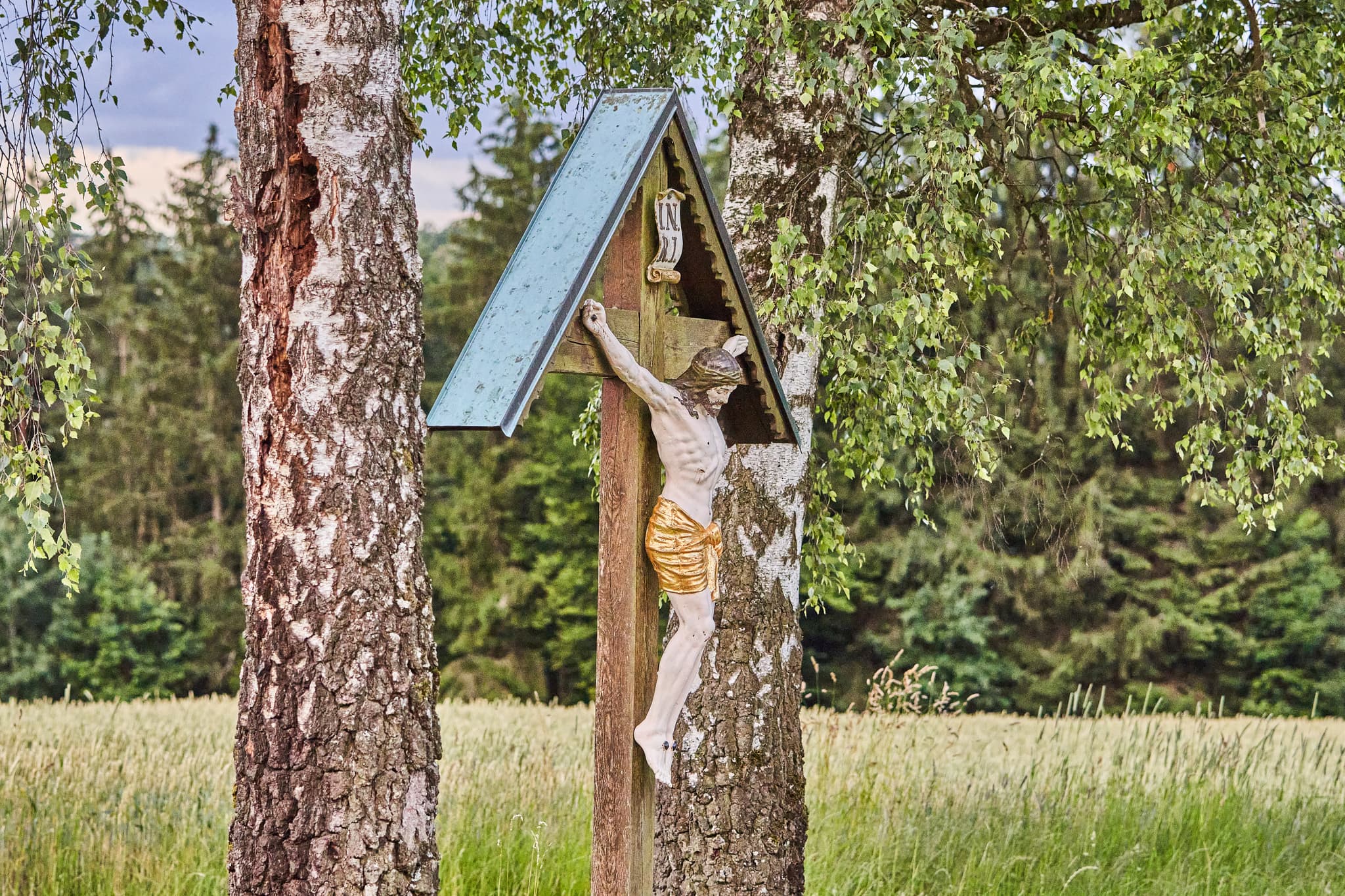 Ein Wegkreuz steht zwischen Birken in ländlicher Umgebung bei Unterfriesing, Reischach, Landkreis Altötting, Oberbayern, Inn-Salzach, Deutschland.
