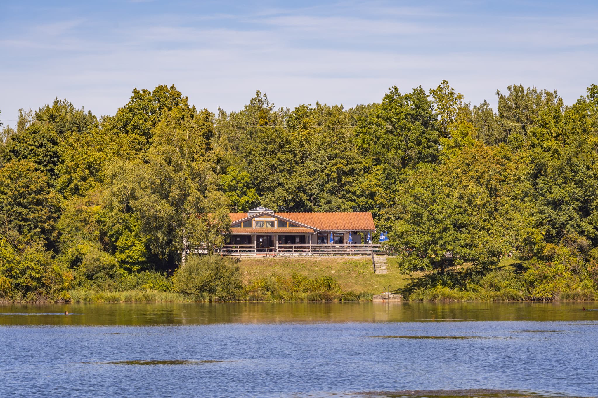 Waldsee Lago Sommer bei Kirchdorf am Inn, Landkreis Rottal-Inn, Niederbayern. Erholsamer Badesee im Bäderdrieck, Deutschland. Umgeben von Wald, Gebäude am Ufer.