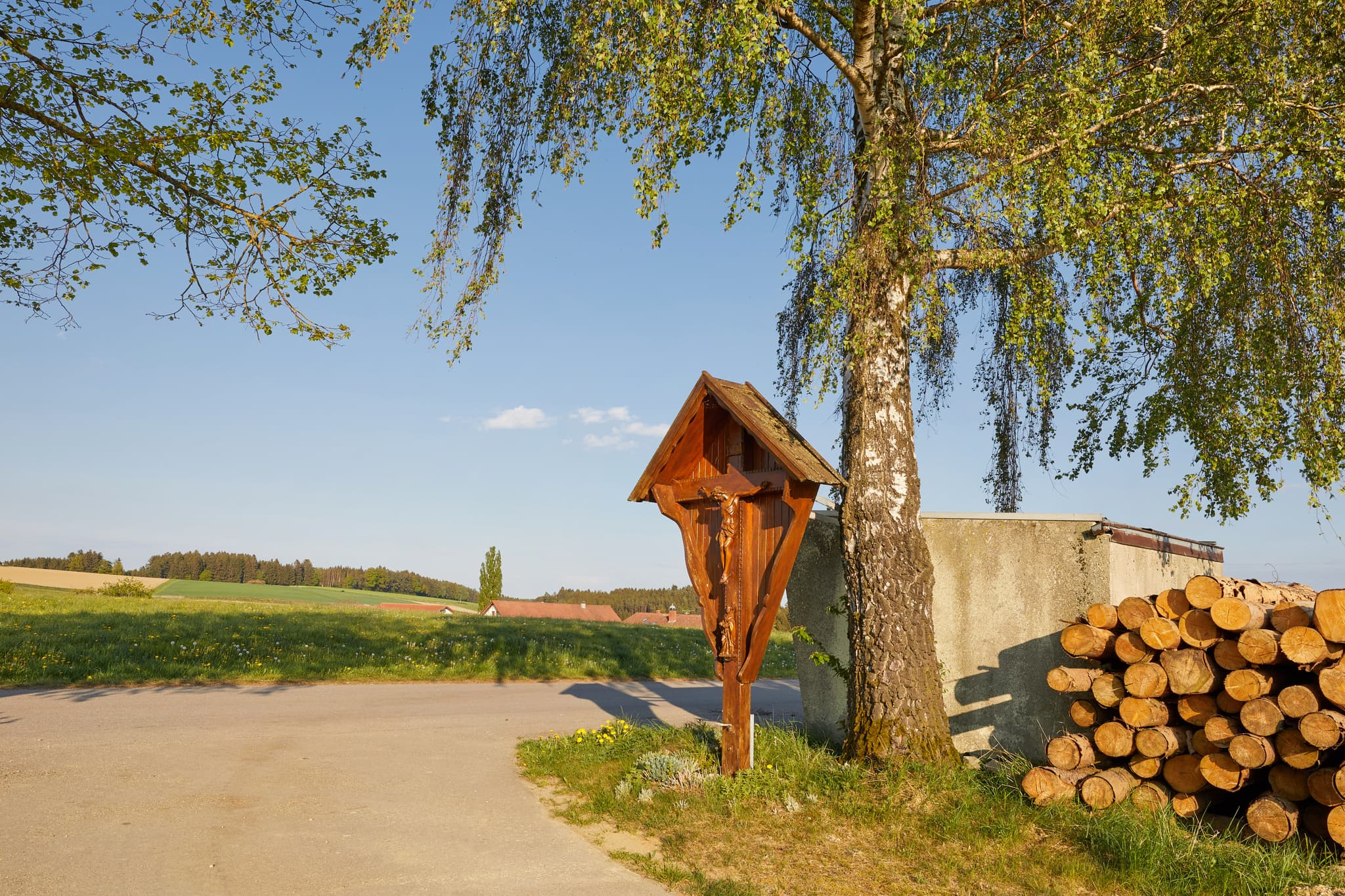 Wegkreuz in Hickerstall, Wurmannsquick, Rottal-Inn, Niederbayern. Motiv: Holzkreuz am Baum, Felder, blauer Himmel. Typische Szene im Holzland, Deutschland.