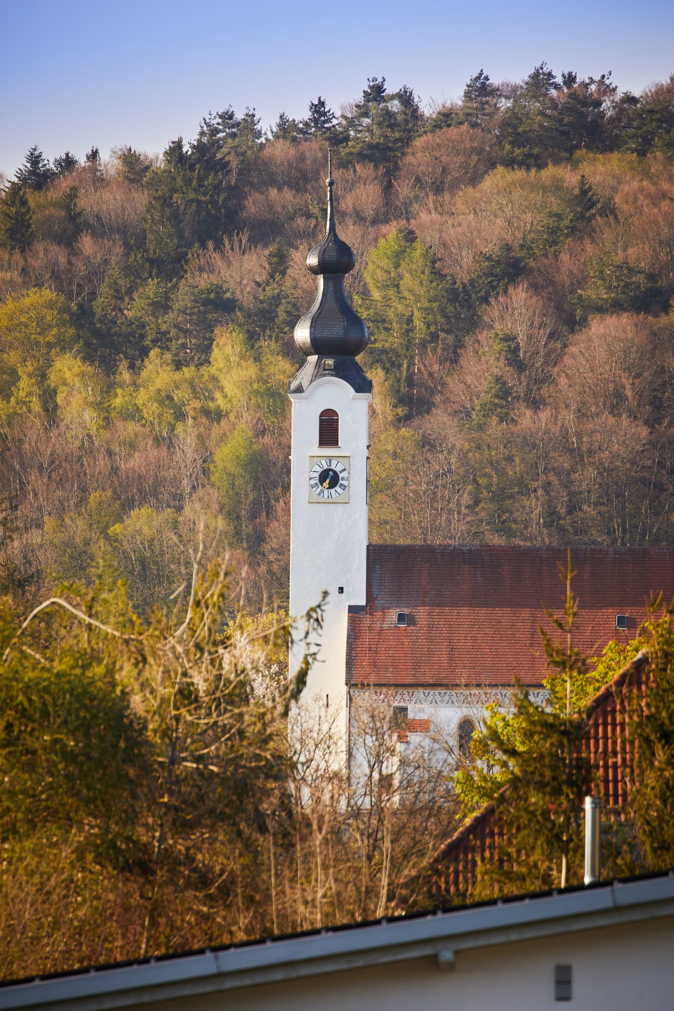 Die Pfarrkirche Mariä Himmelfahrt in Perach, Altötting, Oberbayern, Deutschland. Ein historisches Bauwerk in der Inn-Salzach Region, umgeben von Wald.