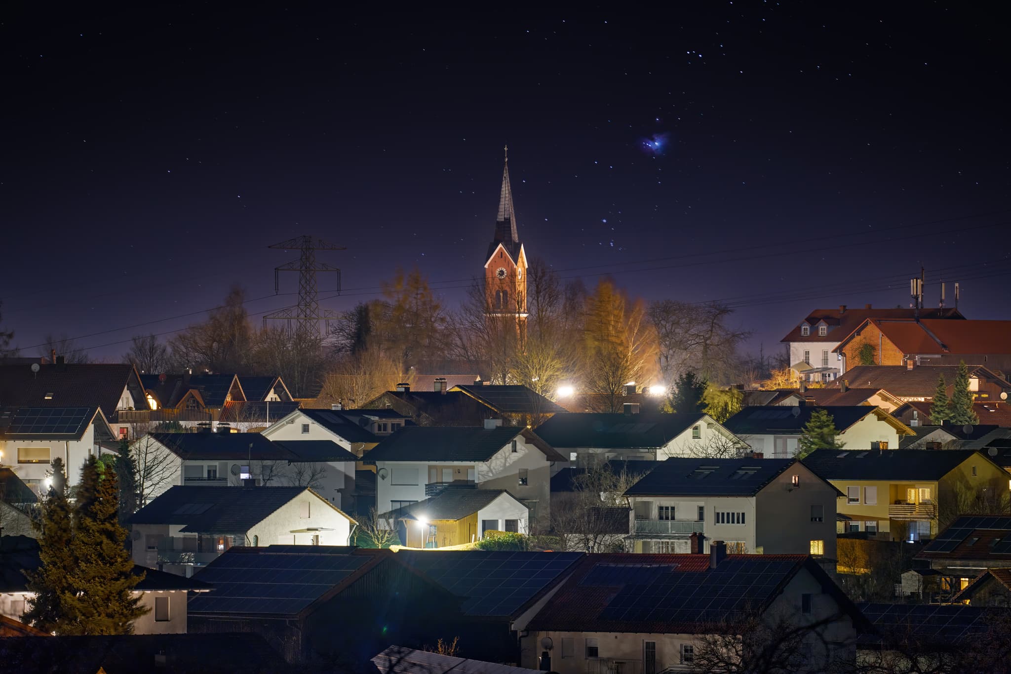 Wurmannsquick im Landkreis Rottal-Inn, Niederbayern, Deutschland, bei Nacht. Eine beleuchtete Ortsansicht mit Kirche und klarem Sternenhimmel mit Orion.