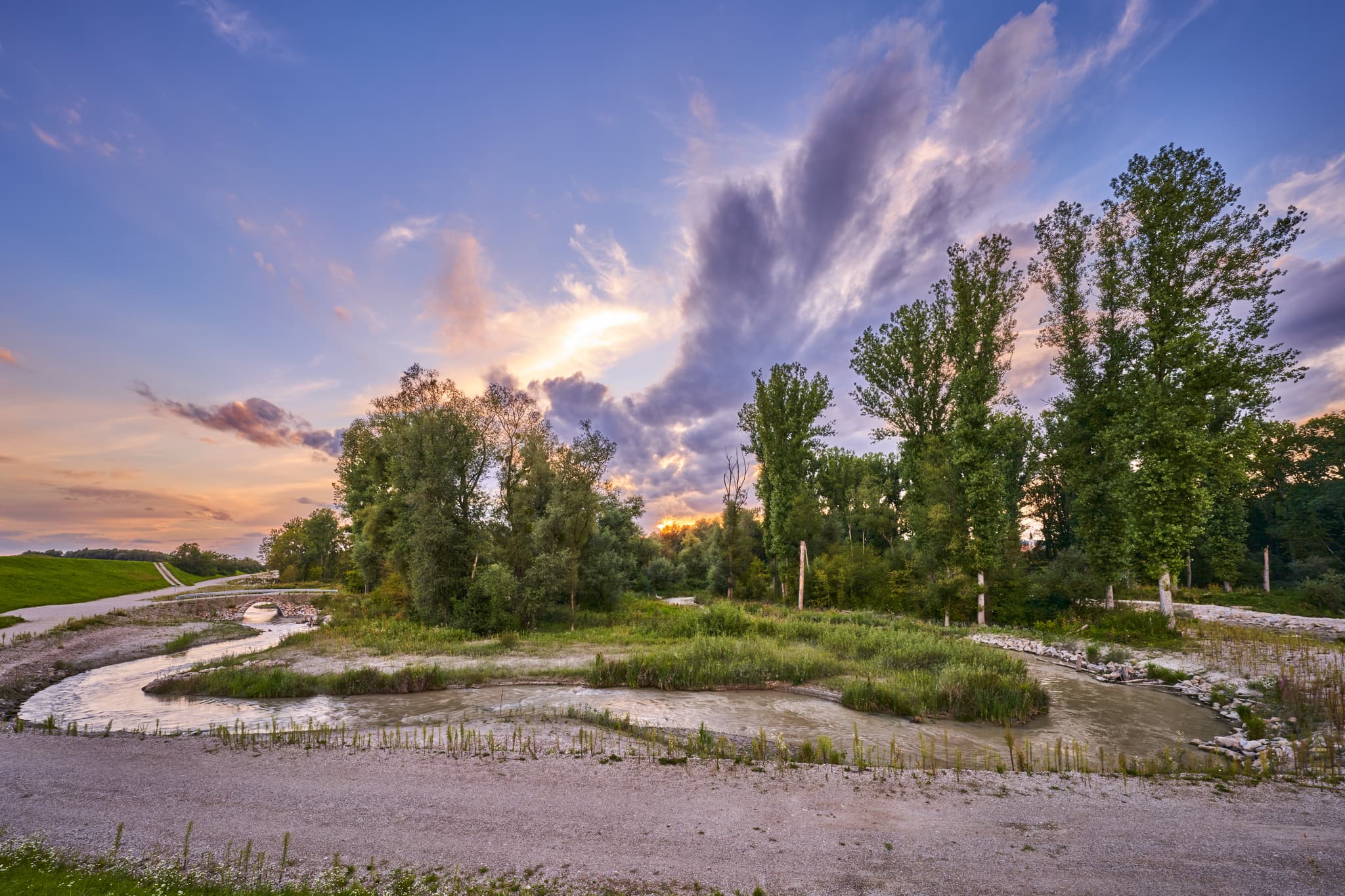 Die Fischwanderhilfe am Inn in Ering, Landkreis Rottal-Inn, Niederbayern, Deutschland. Eine Wasserlandschaft mit Bäumen und einem Brückchen am Inn.
