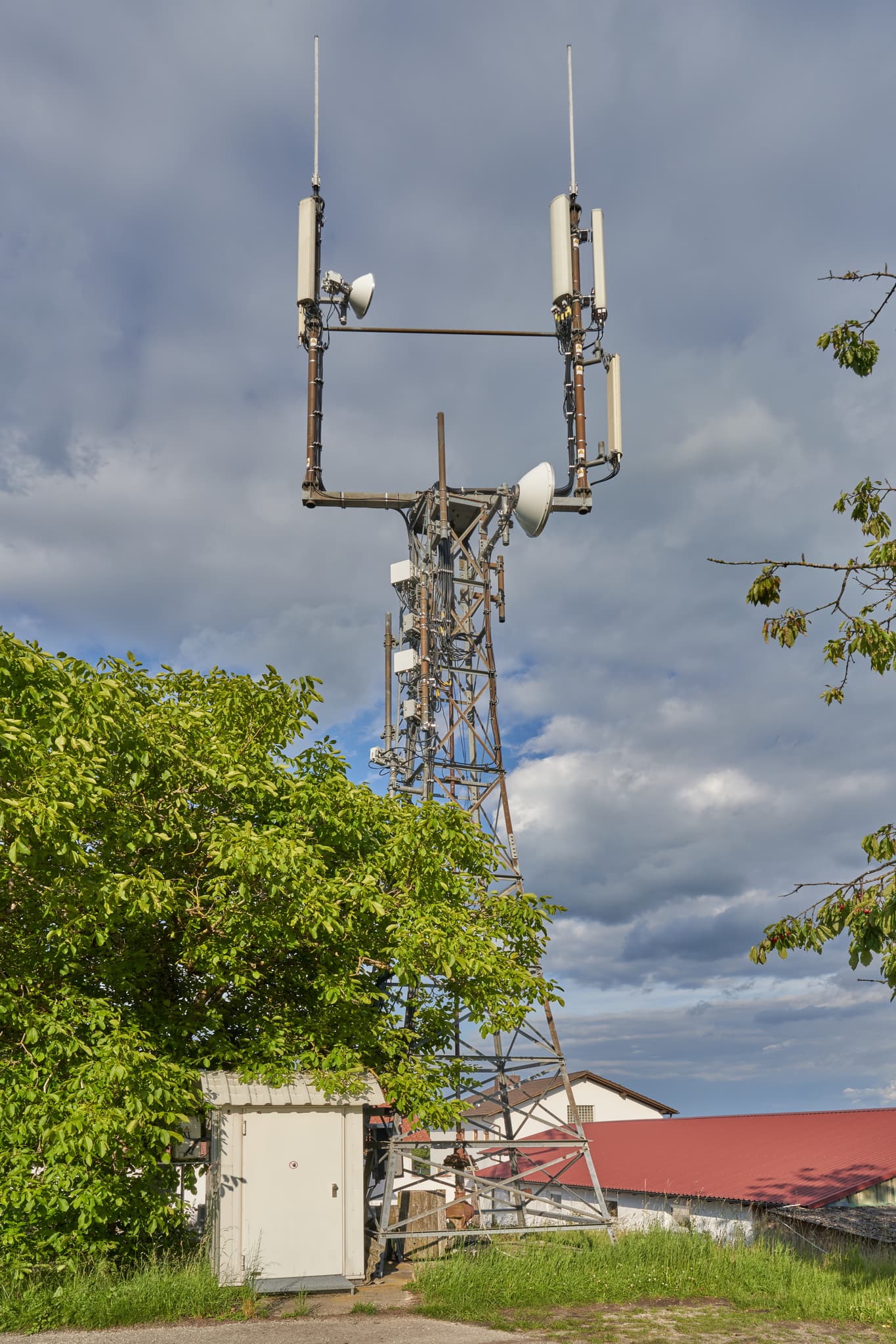 Sendeanlage in Wipfelsberg bei Reischach, Landkreis Altötting, Oberbayern. Funkmast, Betriebsgebäude, Bäume unter bewölktem Himmel.