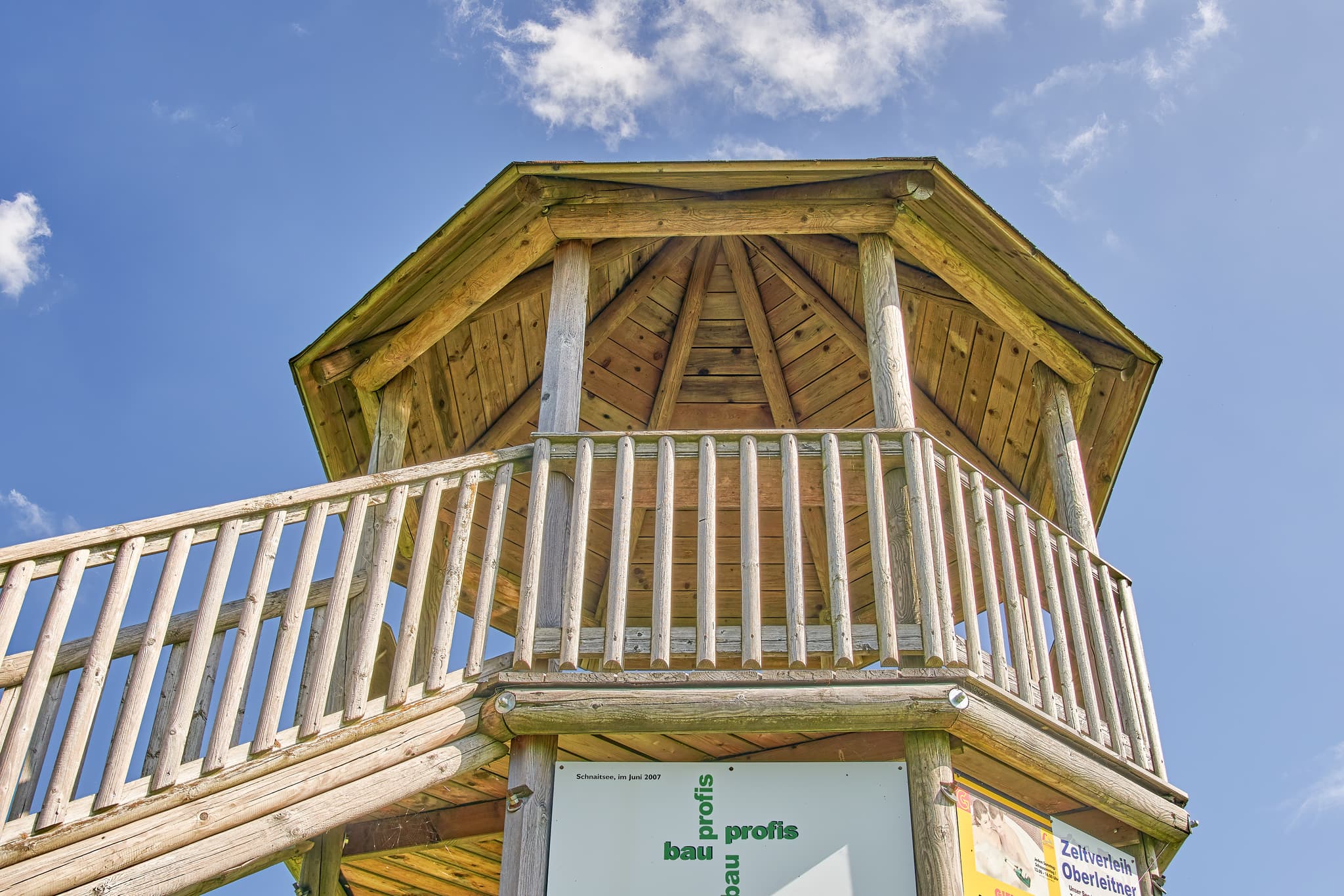 Holz-Aussichtsturm in Schnaitsee, Landkreis Traunstein, Oberbayern, Chiemgau, Deutschland. Ansicht des hölzernen Turms bei blauem Himmel und leichter Bewölkung.