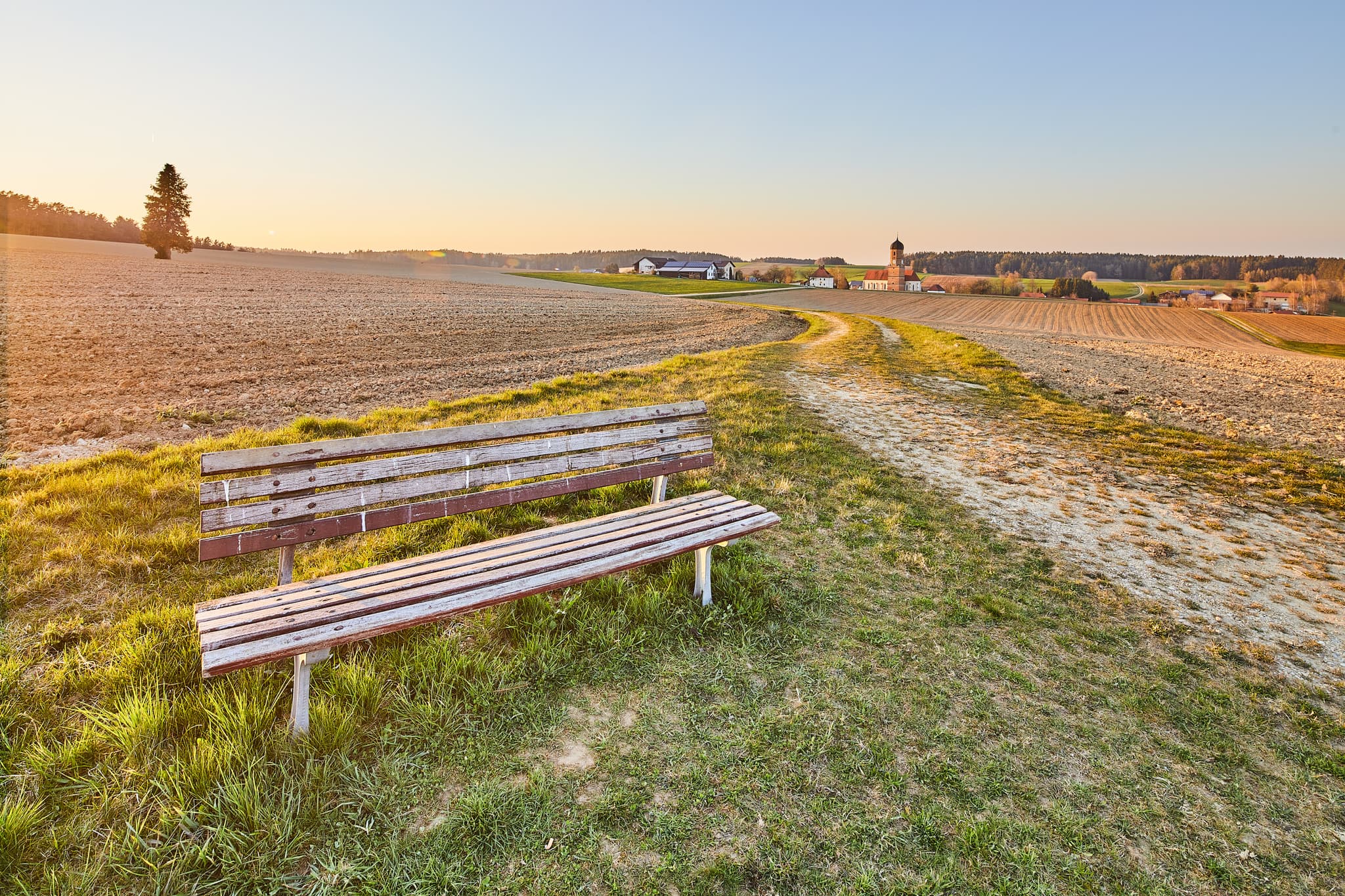Weite Landschaft mit Bank und Dorf im Hintergrund bei Martinskirchen Rogglfing, Wurmannsquick, Landkreis Rottal-Inn, Niederbayern, Deutschland.