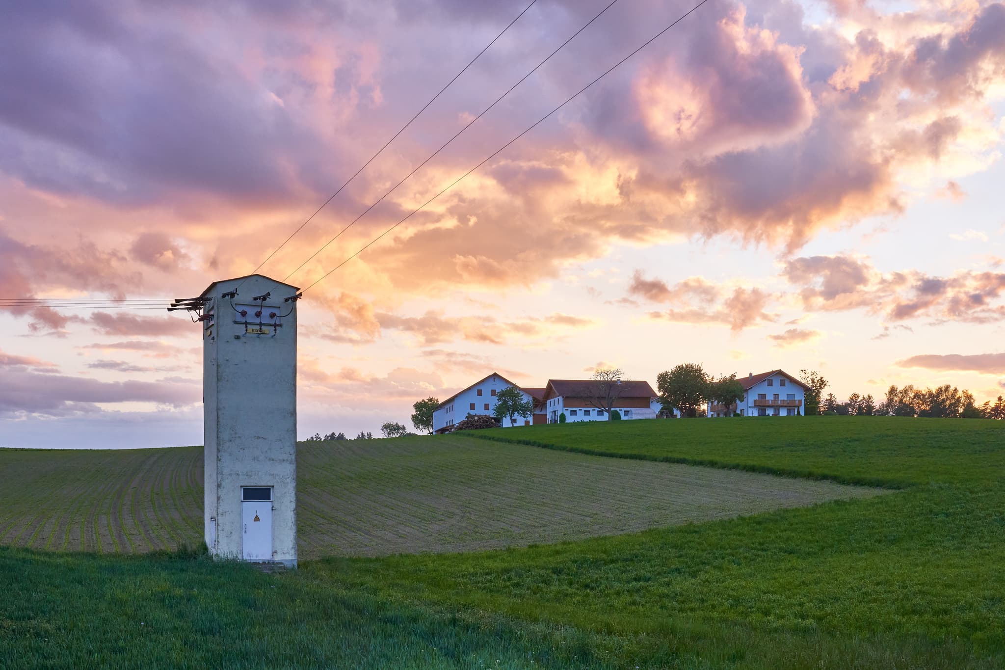 Ländliche Abendlandschaft in Ecking, Reischach, Landkreis Altötting, Oberbayern, Deutschland. Ein Stromverteiler und Bauernhof im Holzland.