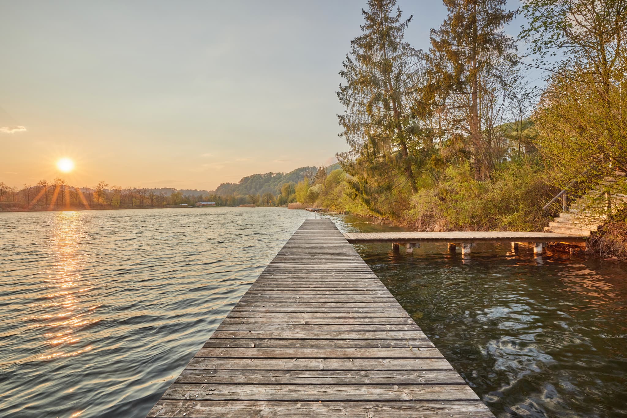 Sonnenuntergang am Marktler Badesee in Oberbayern, Inn-Salzach, Deutschland. Langer Steg am Seeufer. Idyllische Naturlandschaft.