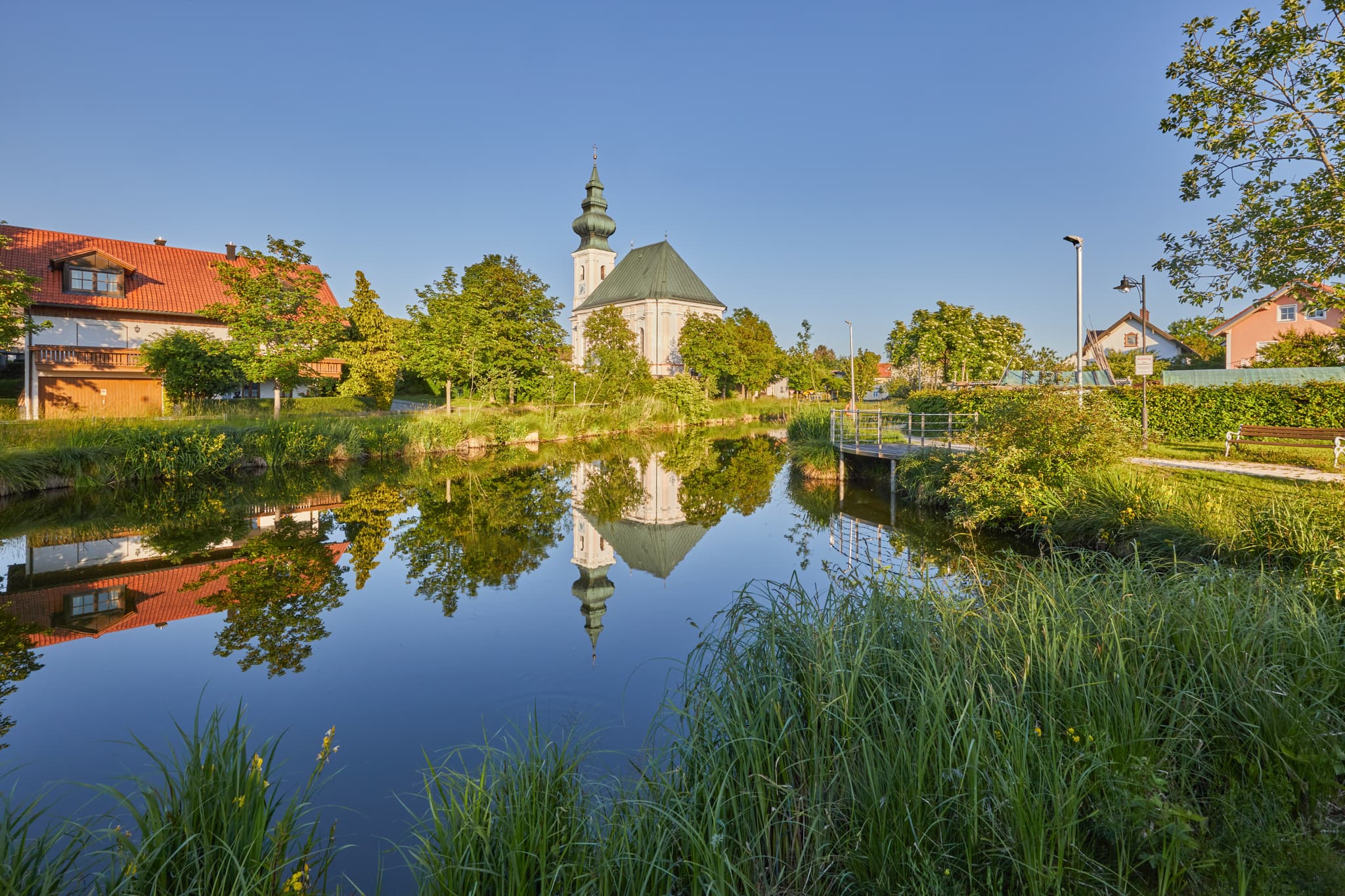 Kirchweidach in Oberbayern, Inn-Salzach, Deutschland: Die Dorfweiher Kirche spiegelt sich idyllisch im Wasser. Ein traumhaftes Fotomotiv in der Region.