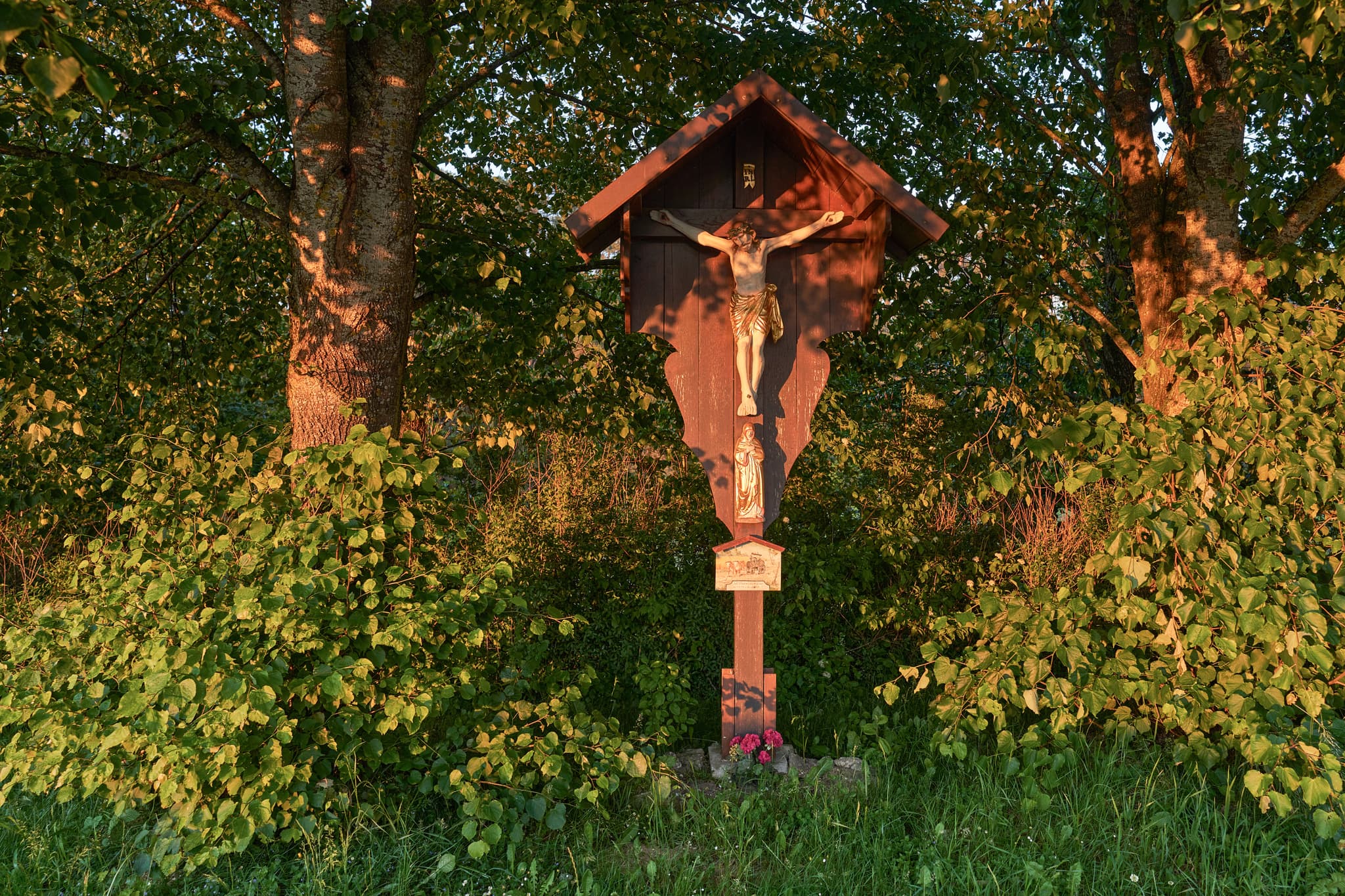 Marterl am Wasserwerk in Hoheneck, Reischach, Landkreis Altötting, Oberbayern. Das Holzwegkreuz steht inmitten grüner Natur. Idyllisch im Sonnenlicht.