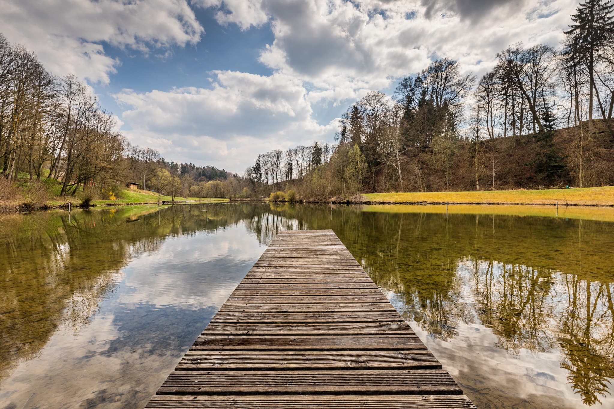 Der Hochmuhl Badesee in Reischach, Landkreis Altötting, liegt in der Region Inn-Salzach in Oberbayern, Deutschland. Holzsteg auf dem ruhigen See.