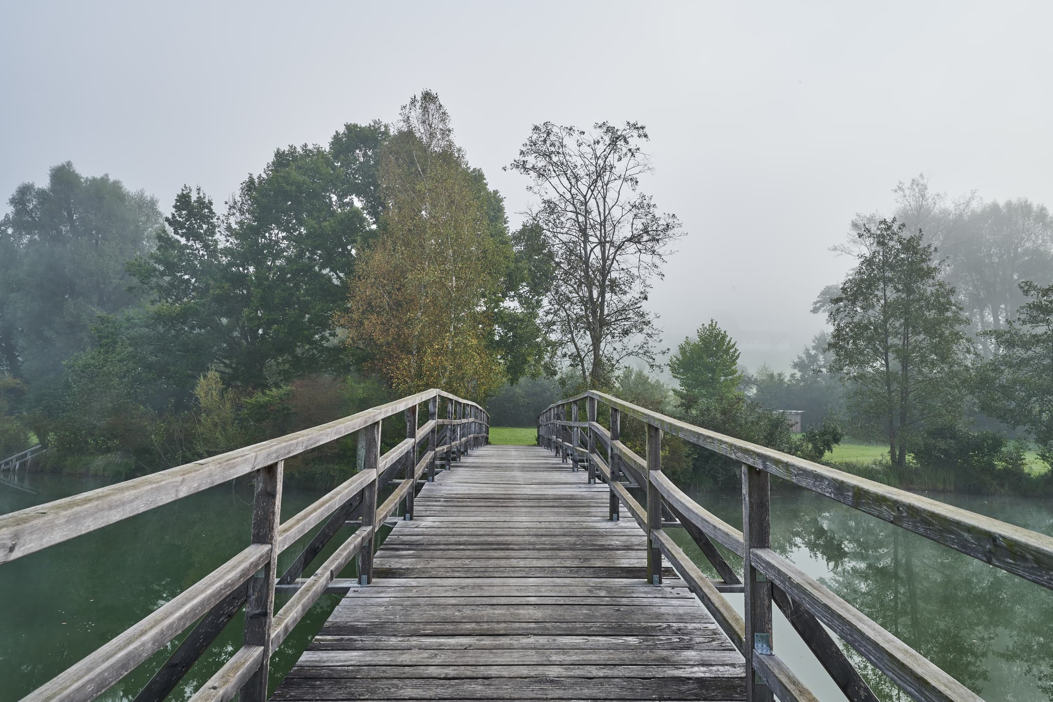 Herbstlicher Morgennebel über dem Badesee in Marktl, Oberbayern, Inn-Salzach, Deutschland. Idyllisches Bild einer Holzbrücke über den See.