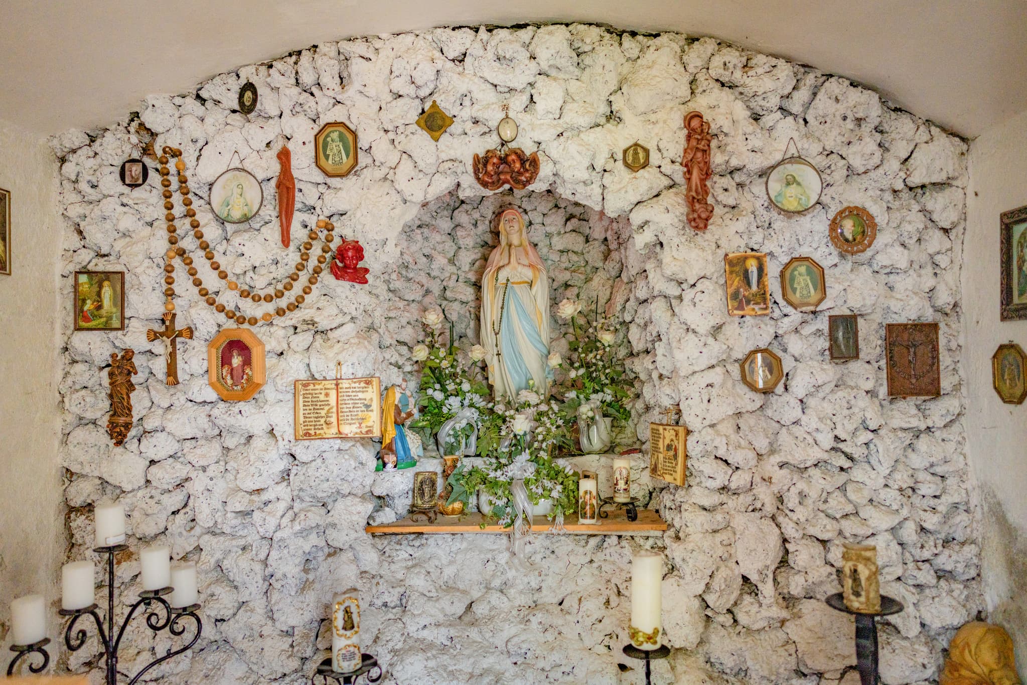 Marienstatue in Kapelle Roßbach, Niedertaufkirchen, Mühldorf am Inn. Kerzen, Rosenkränze, Votivgaben an Steinwand. Religiöse Stätte Oberbayern.