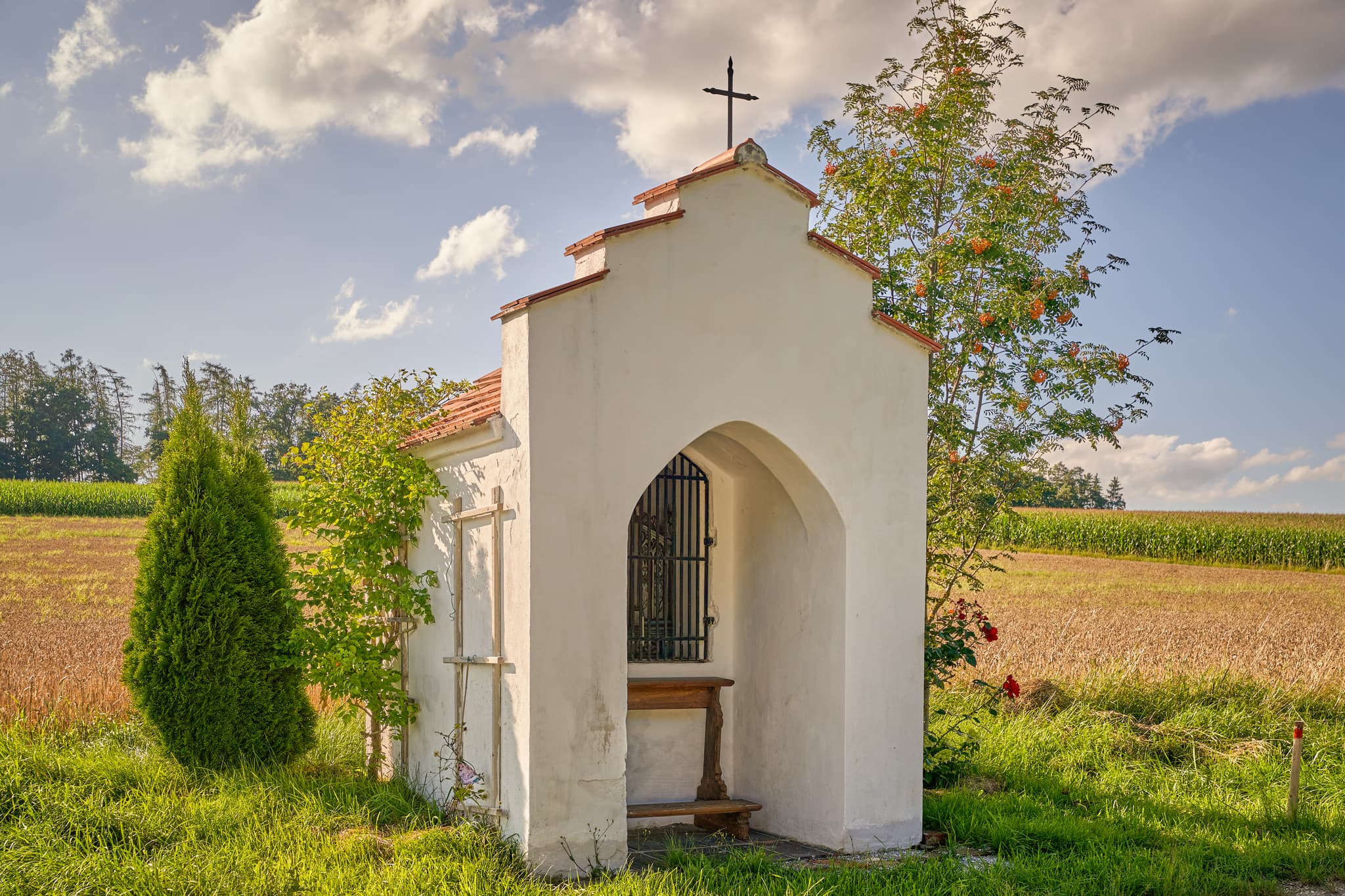 Bildstock am Feldrand in Niedertaufkirchen, Mühldorf am Inn, Oberbayern. Ländliche Szene Inn-Salzach, Deutschland, mit Feldern, Wiesen und blauem Himmel.