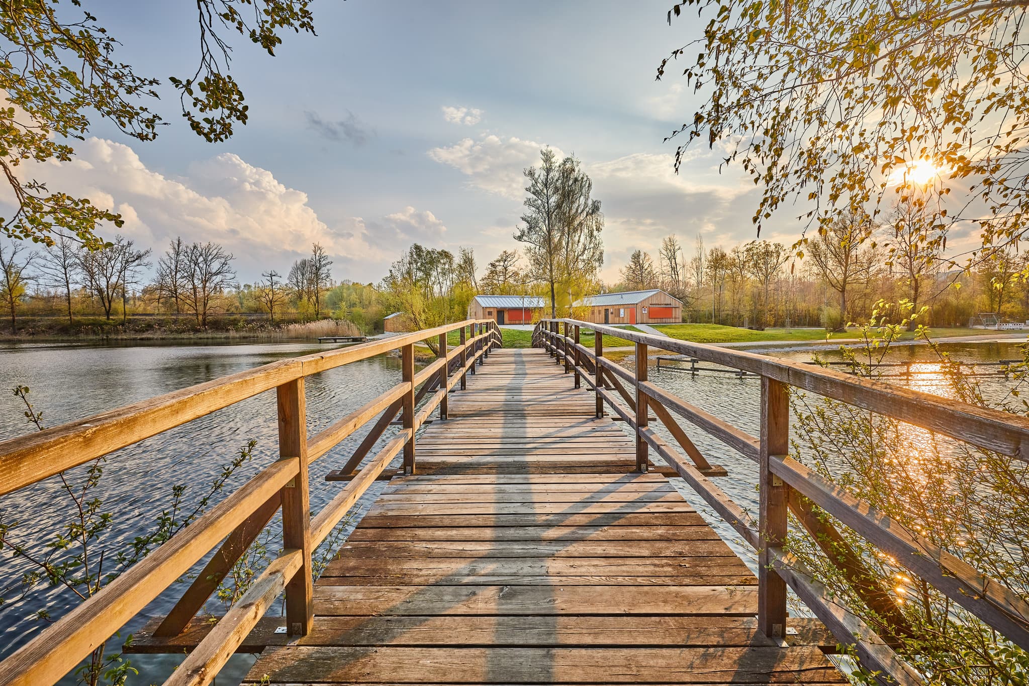 Holzsteg über den Marktler Badesee in Oberbayern, Landkreis Altötting, Region Inn-Salzach, Deutschland. Badesee und Steg bei Sonnenuntergang.