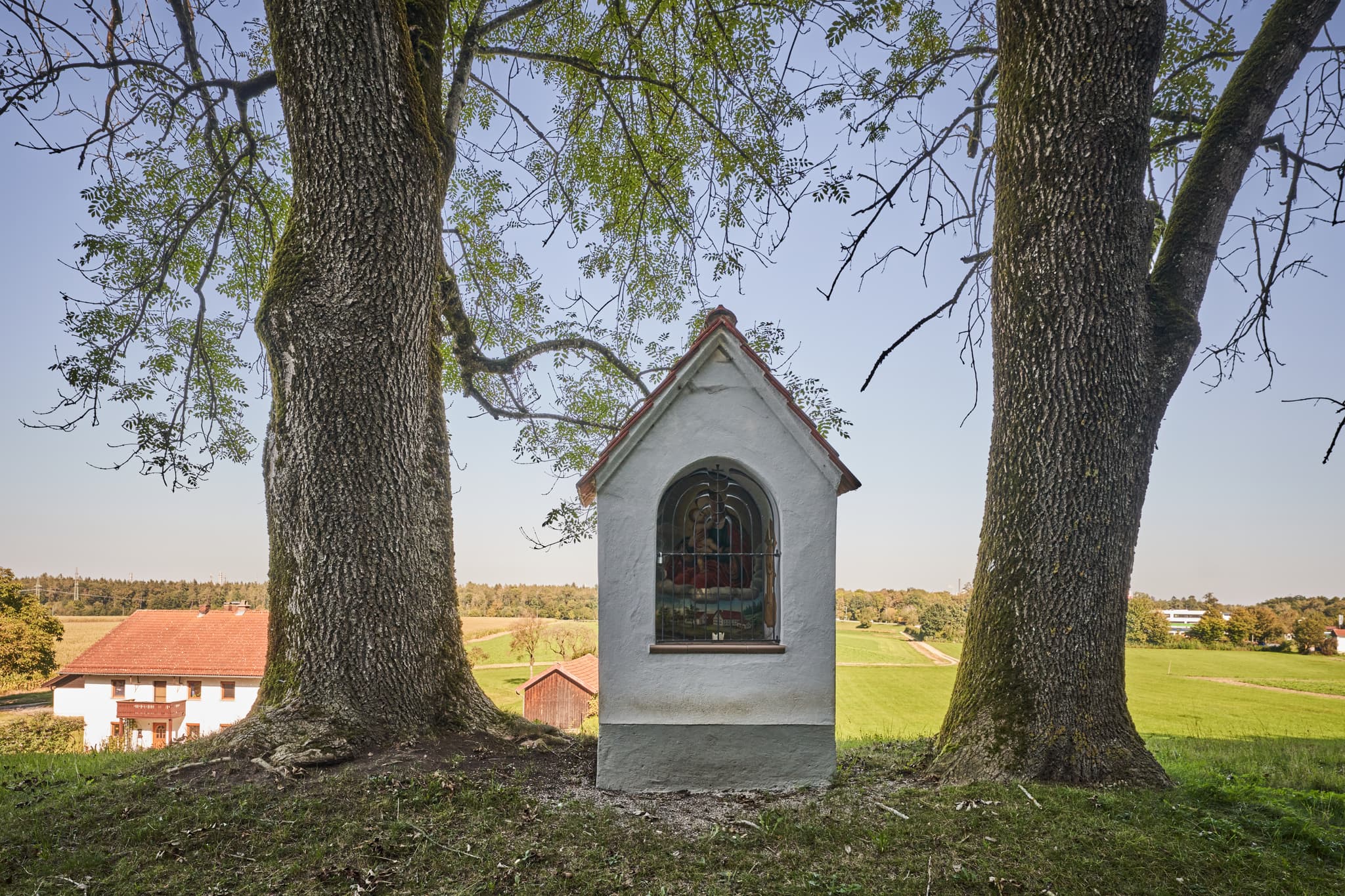 Bildstock am Wolfgangweg in Badhöring, Mehring. Motiv zeigt eine ländliche Szenerie zwischen zwei Bäumen. Landkreis Altötting, Oberbayern, Inn-Salzach.