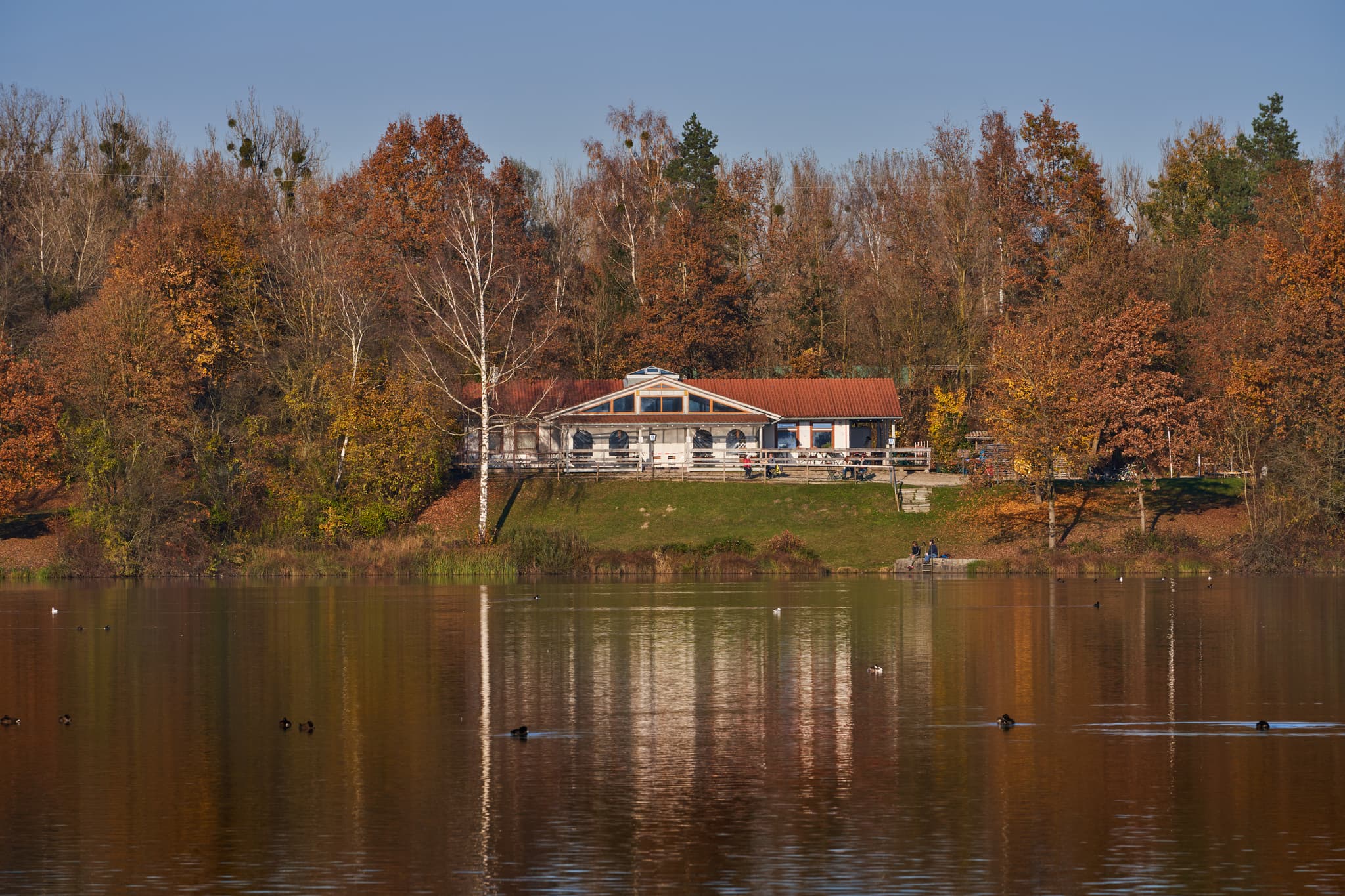 Herbstliche Szene am Waldsee Lago, Kirchdorf am Inn, Rottal-Inn, Niederbayern. Ein Gebäude und Bäume spiegeln sich im See.