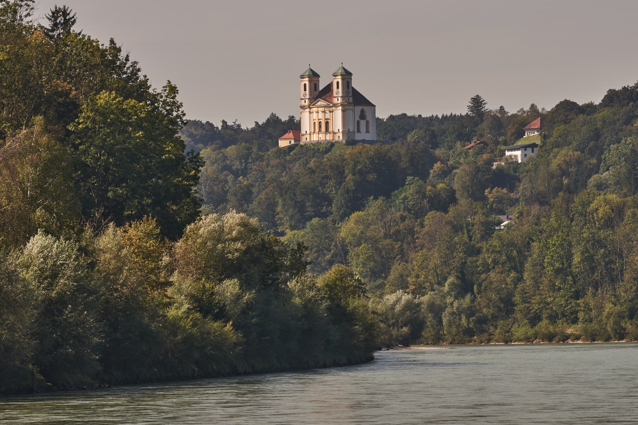 Blick auf die Wallfahrtskirche Marienberg über der Salzach, umgeben von dicht bewaldeten Hügeln nahe Burghausen im Landkreis Altötting.