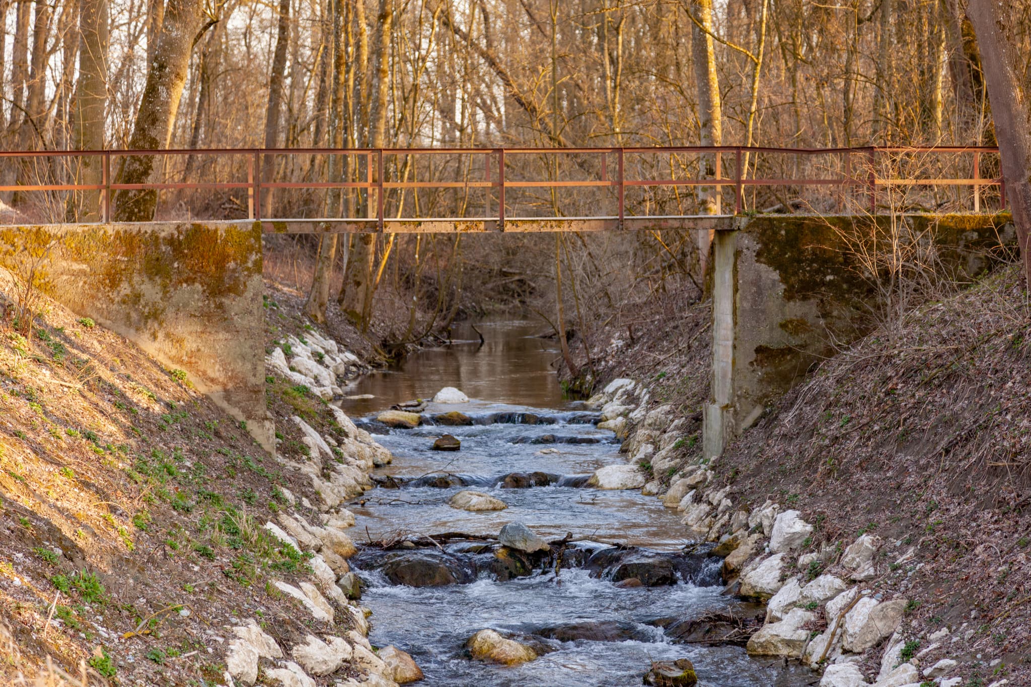 Idyllische Flusslandschaft in Mühldorf am Inn, Oberbayern. Ein kleiner Bach verläuft unter einer Brücke, umgeben von Natur im Inn-Salzach-Gebiet Deutschlands.