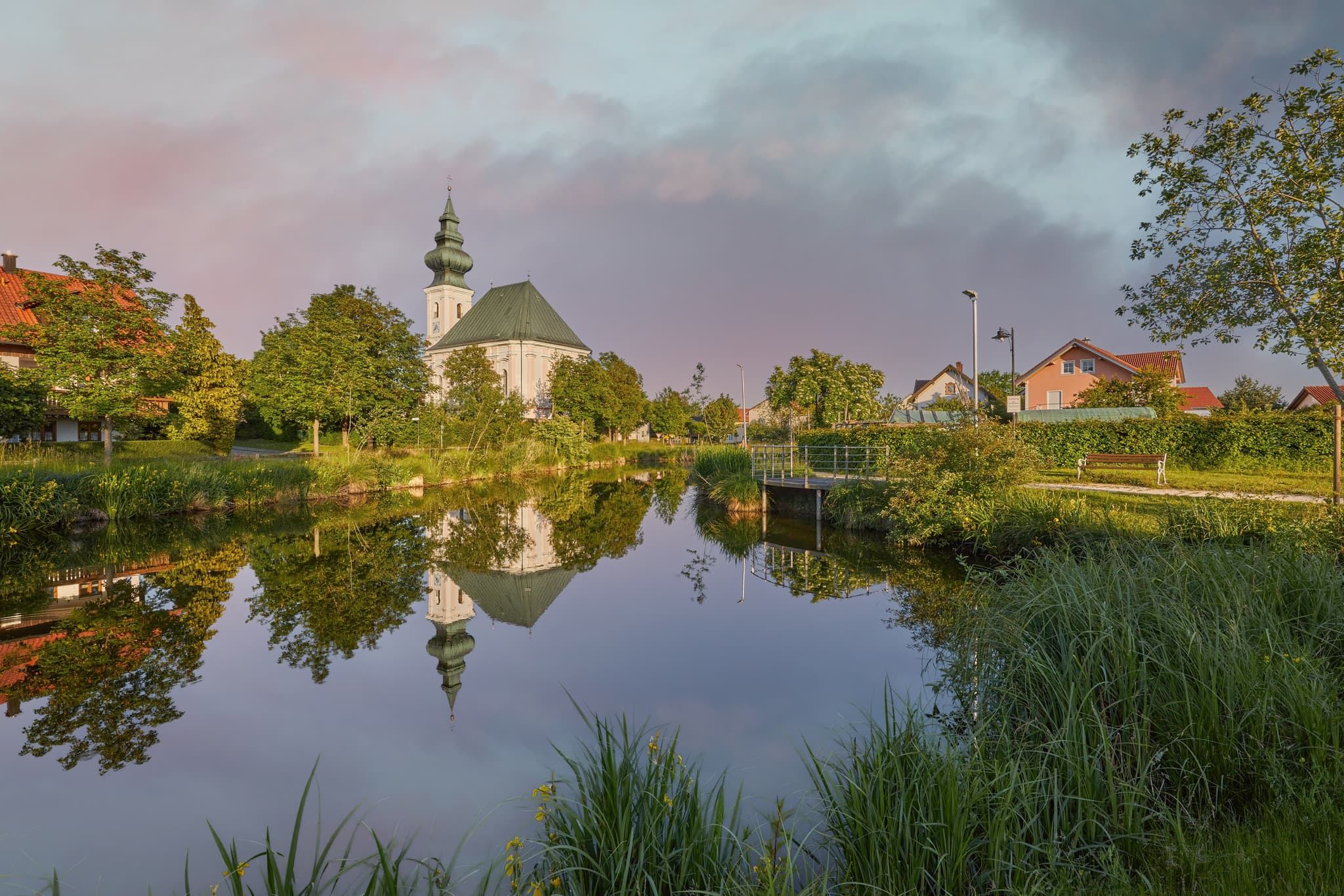 Idyllische Dorfweiher Kirche in Kirchweidach, Oberbayern, im Inn-Salzach Gebiet, Deutschland. Ein malerisches Motiv mit Spiegelung im Wasser.