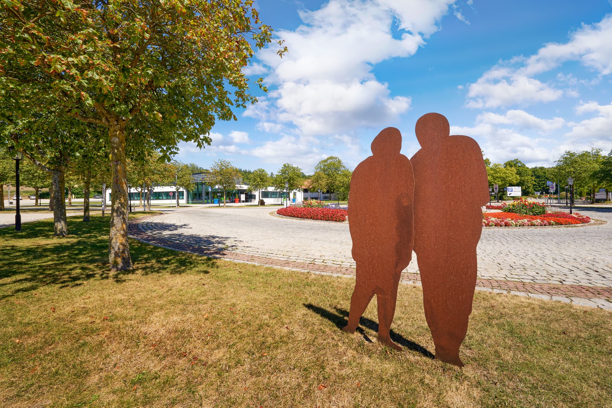 Rostige Skulptur am Therme Kreisverkehr in Bad Griesbach, Landkreis Passau. Darstellung eines Paares vor Gebäuden und Grünflächen in Niederbayern, Deutschland.