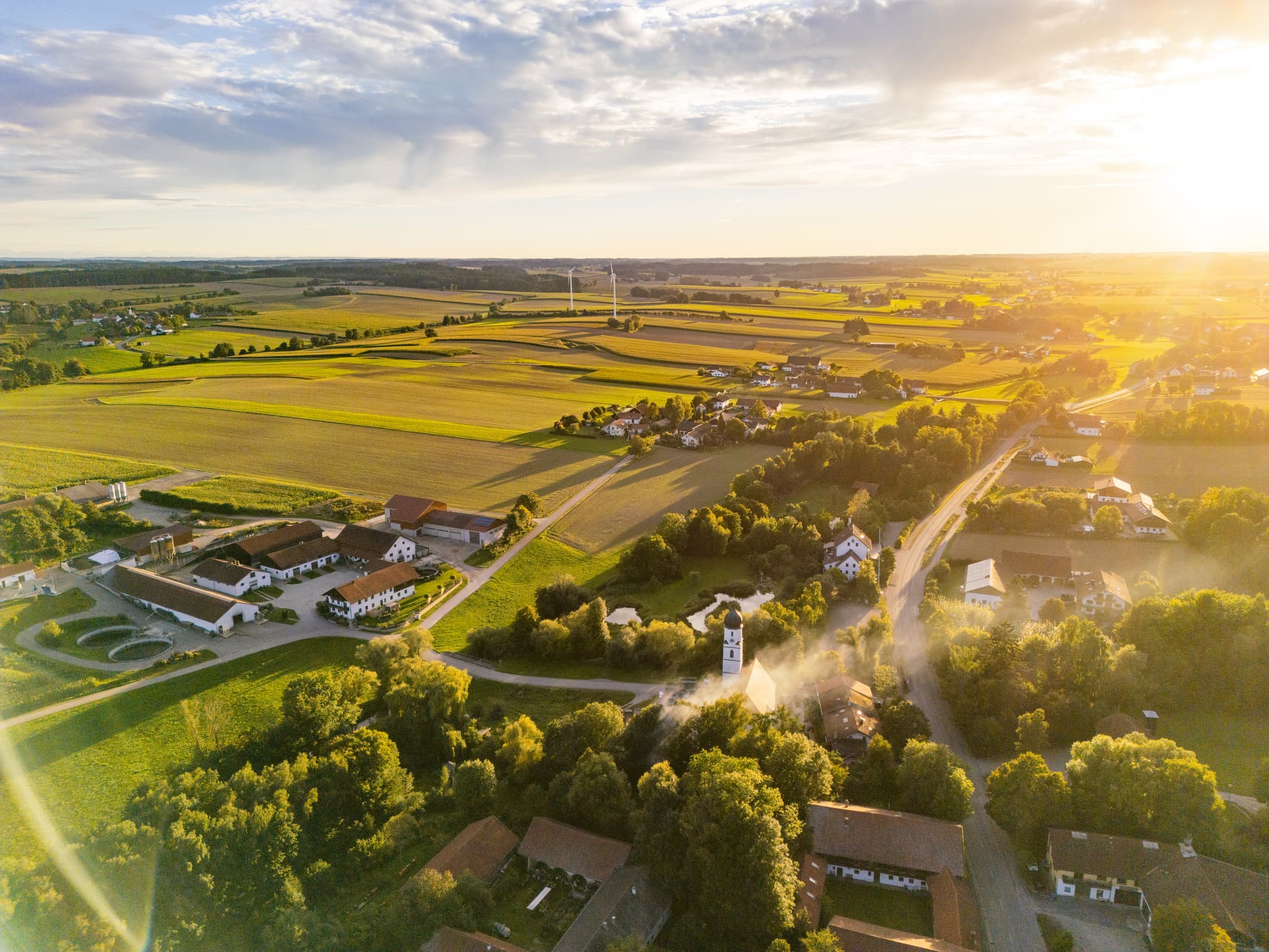 Ortsansicht Dirnaich, Gangkofen, Rottal-Inn, Niederbayern. Ein Windpark prägt die Landschaft im Holzland. Weite Felder unter Sonnenuntergang in Deutschland.