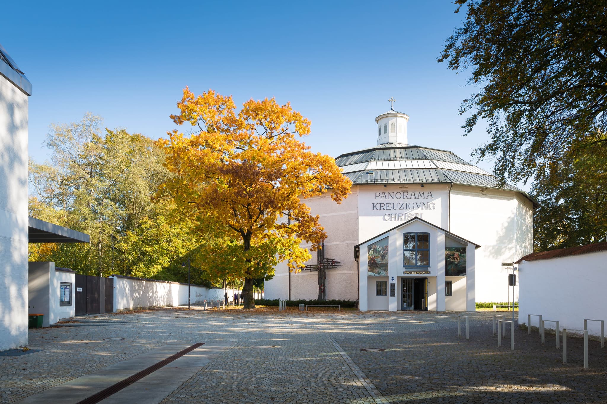 Das Panorama Kreuzigung Christi in Altötting, Landkreis Altötting, Oberbayern, Inn-Salzach, Deutschland. Rundbau mit Herbstbaum und Vorplatz.