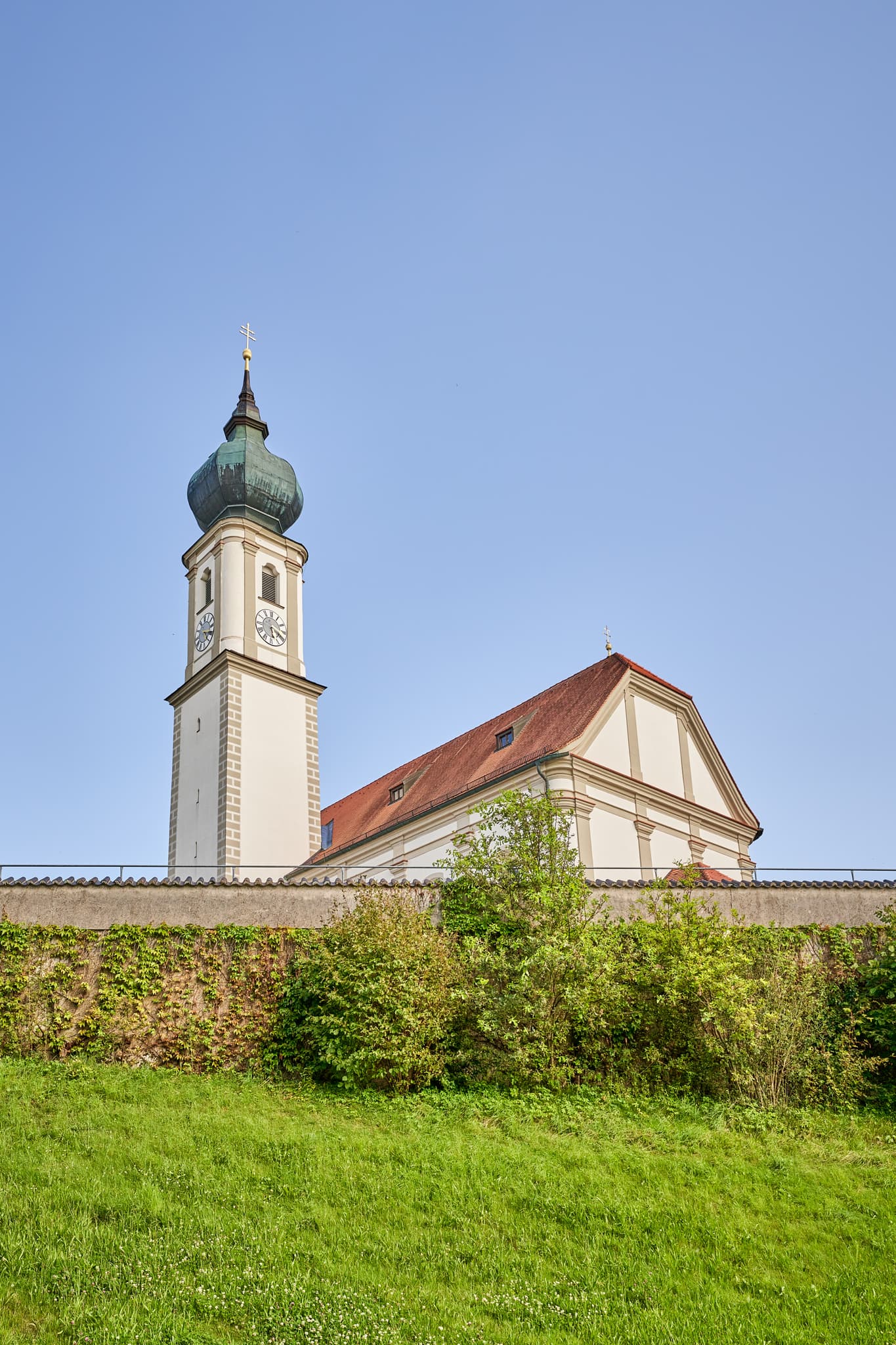 Kirche St. Martin, Niedertaufkirchen, Mühldorf am Inn, Oberbayern, Inn-Salzach. Historisches Gotteshaus mit Zwiebelturm und Mauer. Grüne Wiese, blauer Himmel.