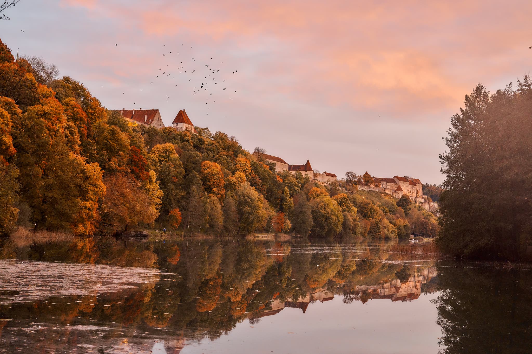 Herbstliche Landschaft am Wöhrsee in Burghausen, Altötting, Oberbayern, Deutschland. Historische Gebäude der Burg spiegeln sich im See.