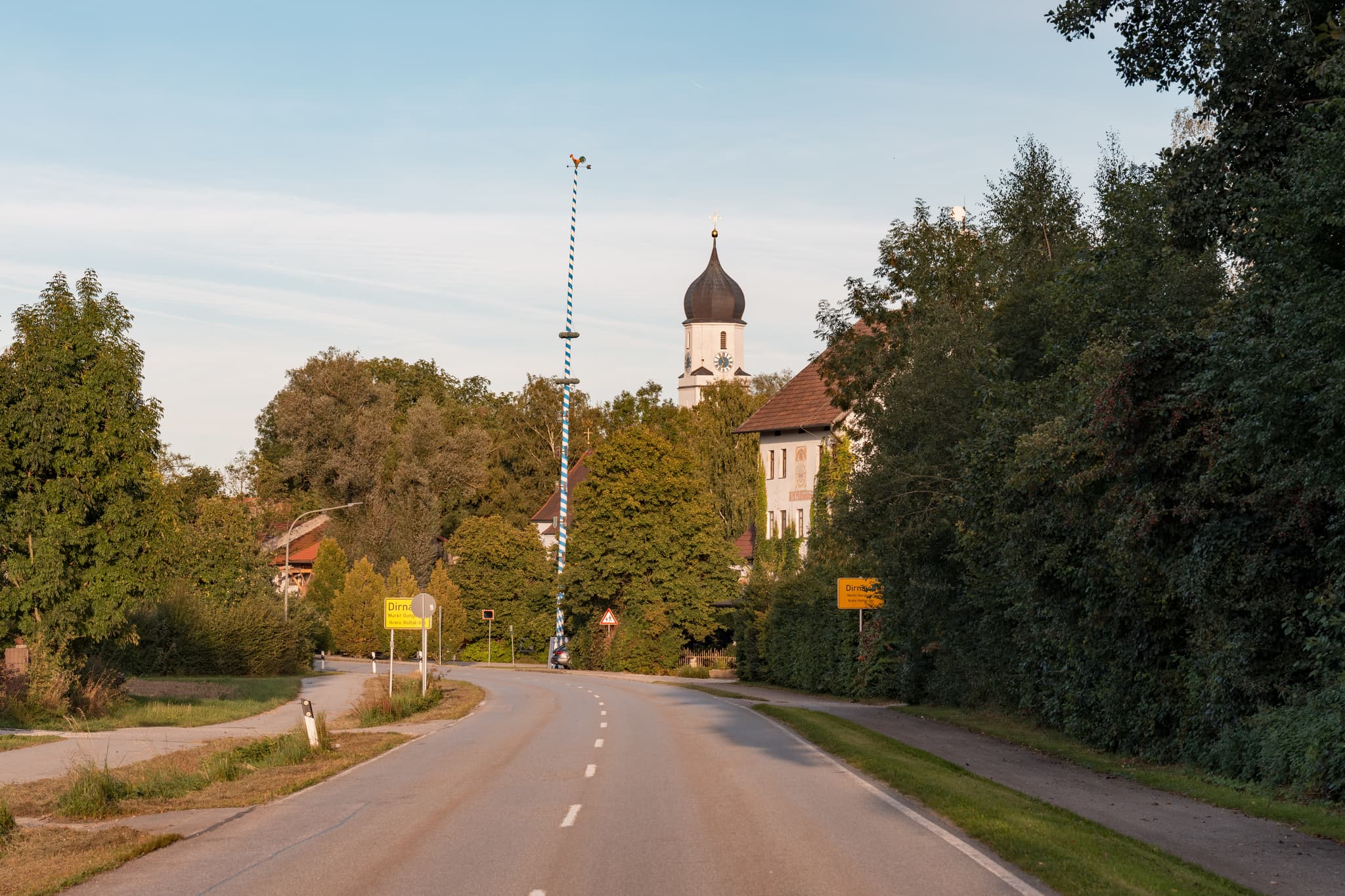 Ortseingang Dirnaich, Ortsteil Gangkofen, Landkreis Rottal-Inn, Niederbayern. Ansicht mit Maibaum, Kirchturm und bewaldeter Landschaft im Holzland, Deutschland.