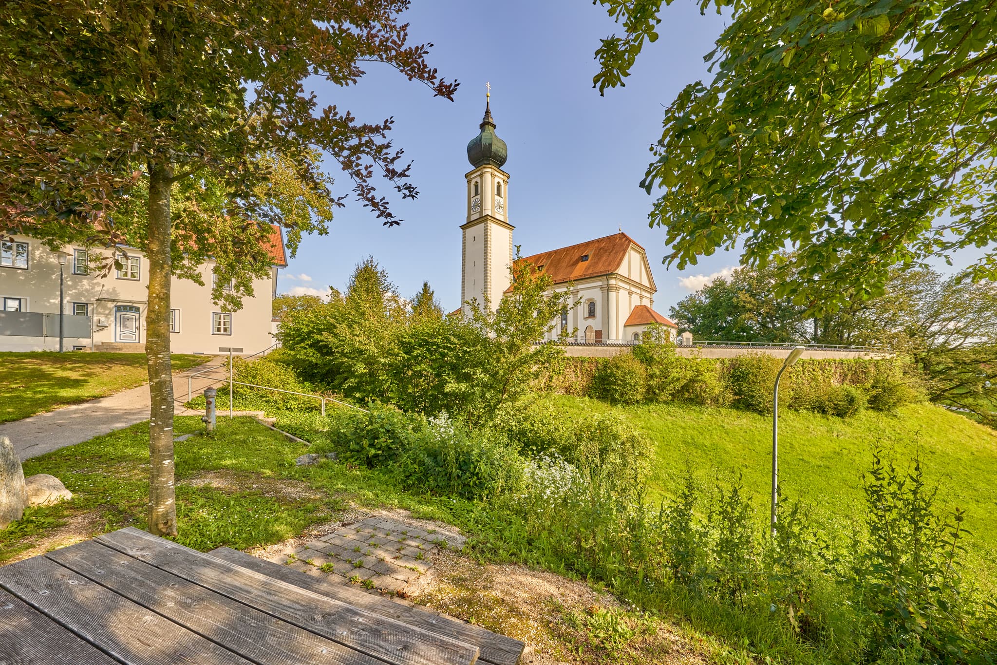 Kirche St. Martin, Niedertaufkirchen, Mühldorf am Inn, Oberbayern, Inn-Salzach. Historisches Gotteshaus mit Zwiebelturm und Mauer. Grüne Wiese, blauer Himmel.
