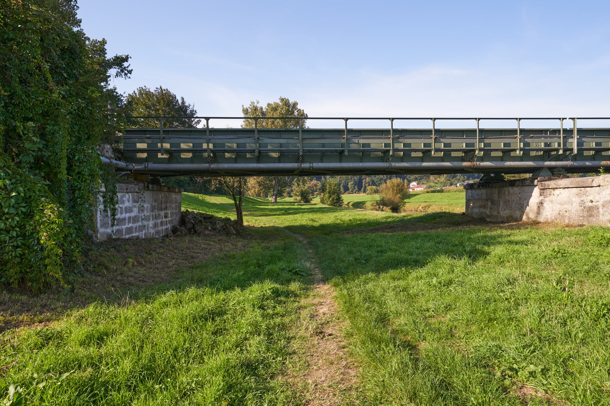 Eine grüne Metallbrücke überquert einen Feldweg und die Isen bei Kronberg, Winhöring. Landkreis Altötting, Oberbayern, Inn-Salzach, Deutschland.