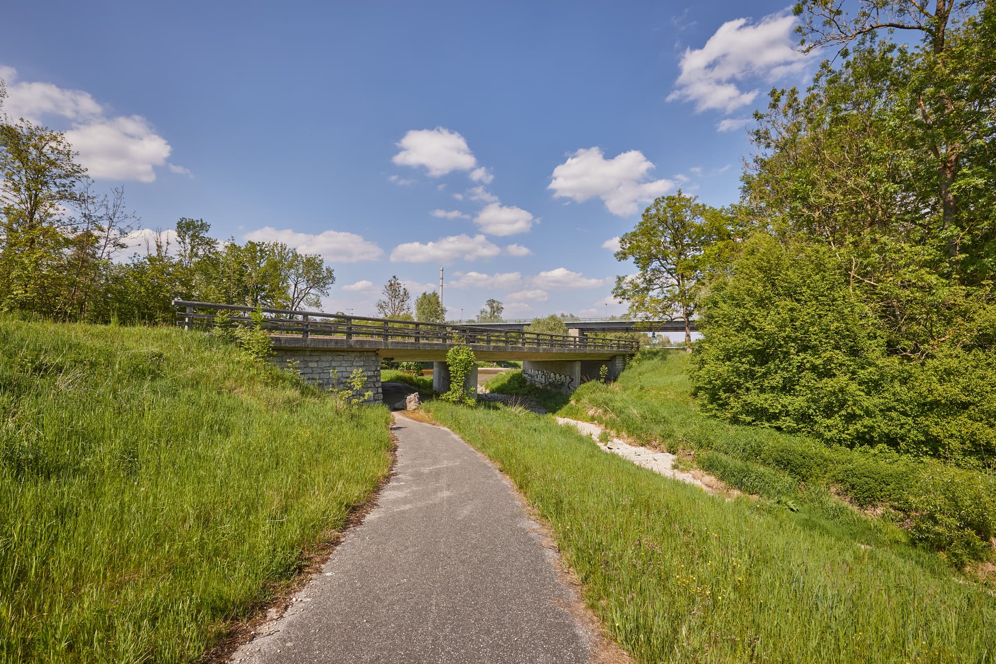 Radweg unter Brücke, umgeben von Wiesen und Bäumen. Ansicht bei Burgkirchen, Landkreis Altötting, Oberbayern. Landschaft der Region Inn-Salzach