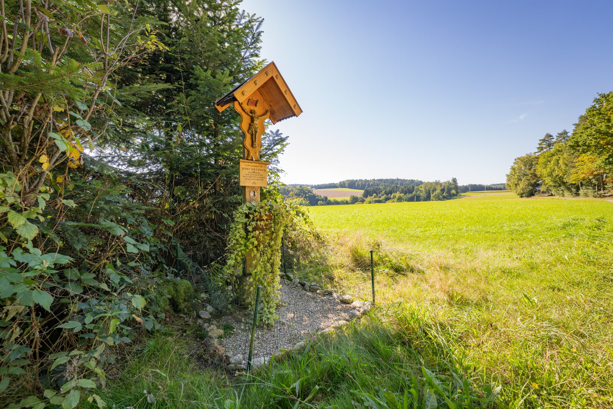 Ein Holzkreuz steht am Feldrand in Guteneck, Johanniskirchen, Rottal-Inn, Niederbayern, Deutschland, Holzland-Landschaft mit weiten Feldern und Wäldern.
