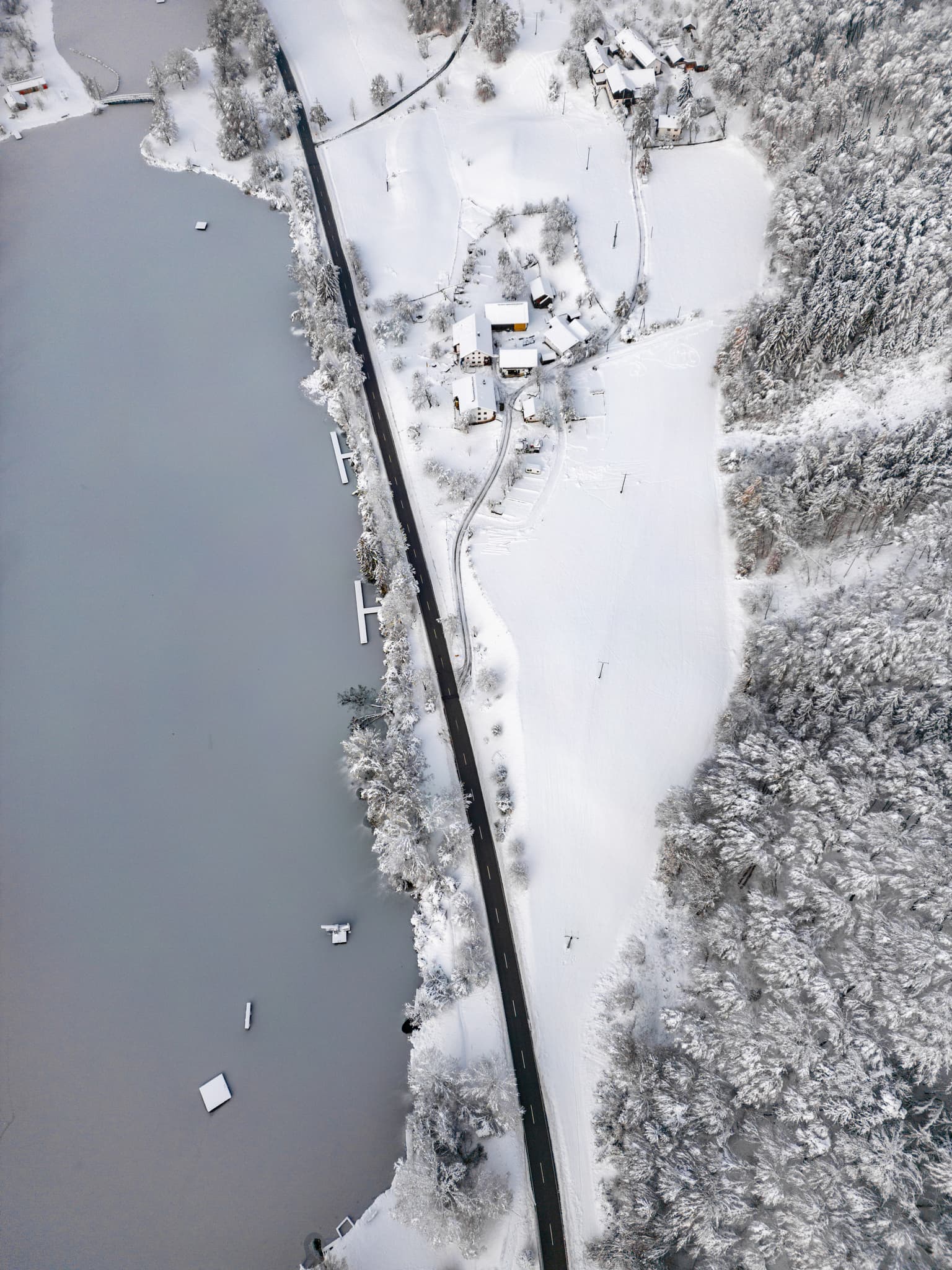 Badesee in Marktl, Landkreis Altötting, Oberbayern, Inn-Salzach, Deutschland. Die winterliche Landschaft zeigt See, Straße und schneebedeckte Umgebung.