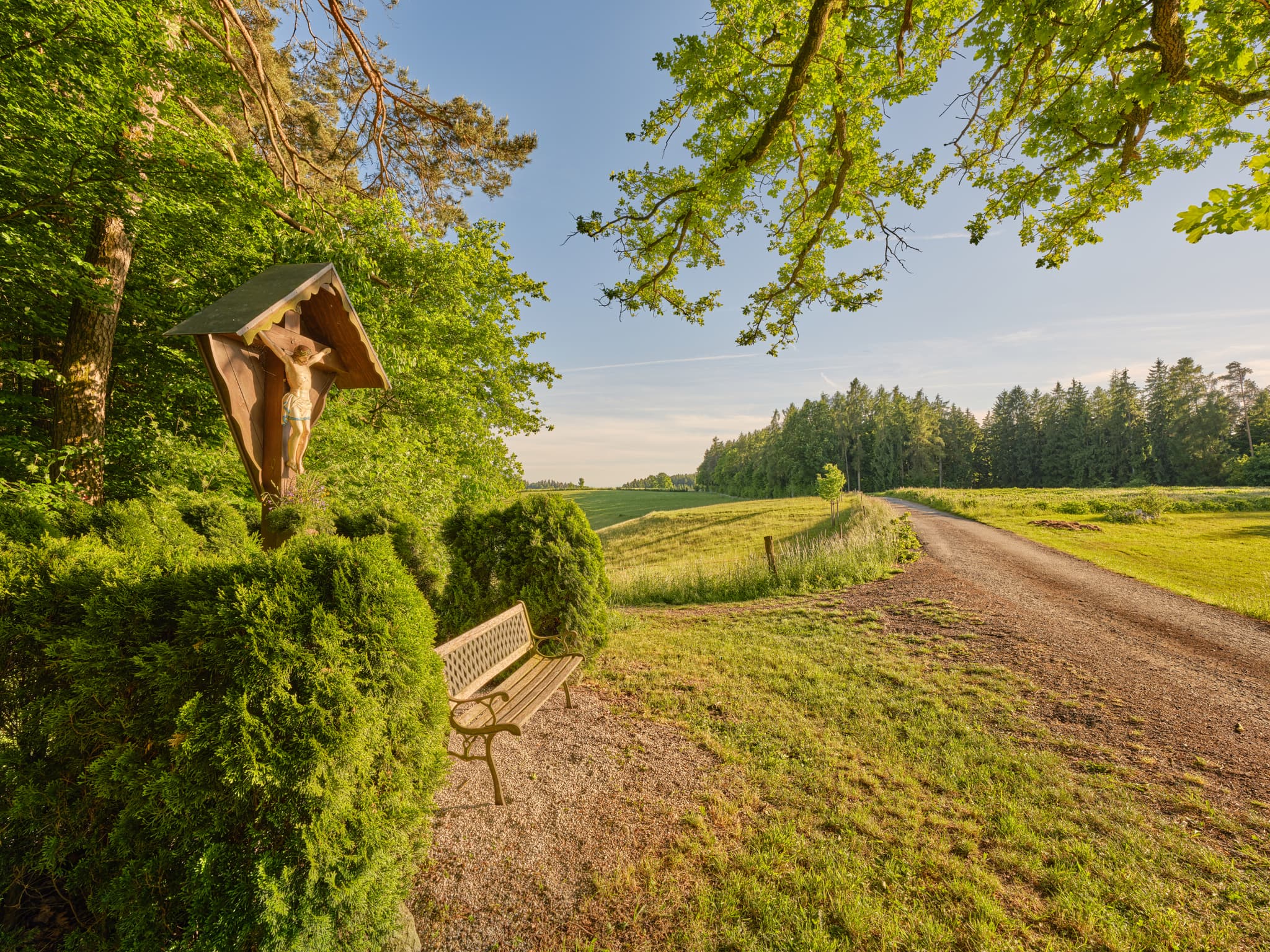 Daxl Wegkreuz und Sitzbank am Feldweg in Waldberg, Reischach, Altötting, Oberbayern, Inn-Salzach, Deutschland. Natur und Wald prägen die ländliche Landschaft.