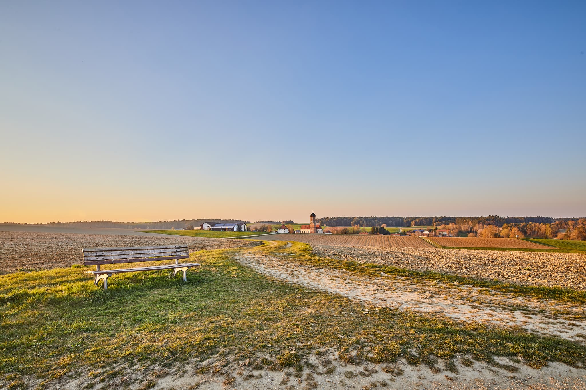 Weite Landschaft mit Bank und Dorf im Hintergrund bei Martinskirchen Rogglfing, Wurmannsquick, Landkreis Rottal-Inn, Niederbayern, Deutschland.