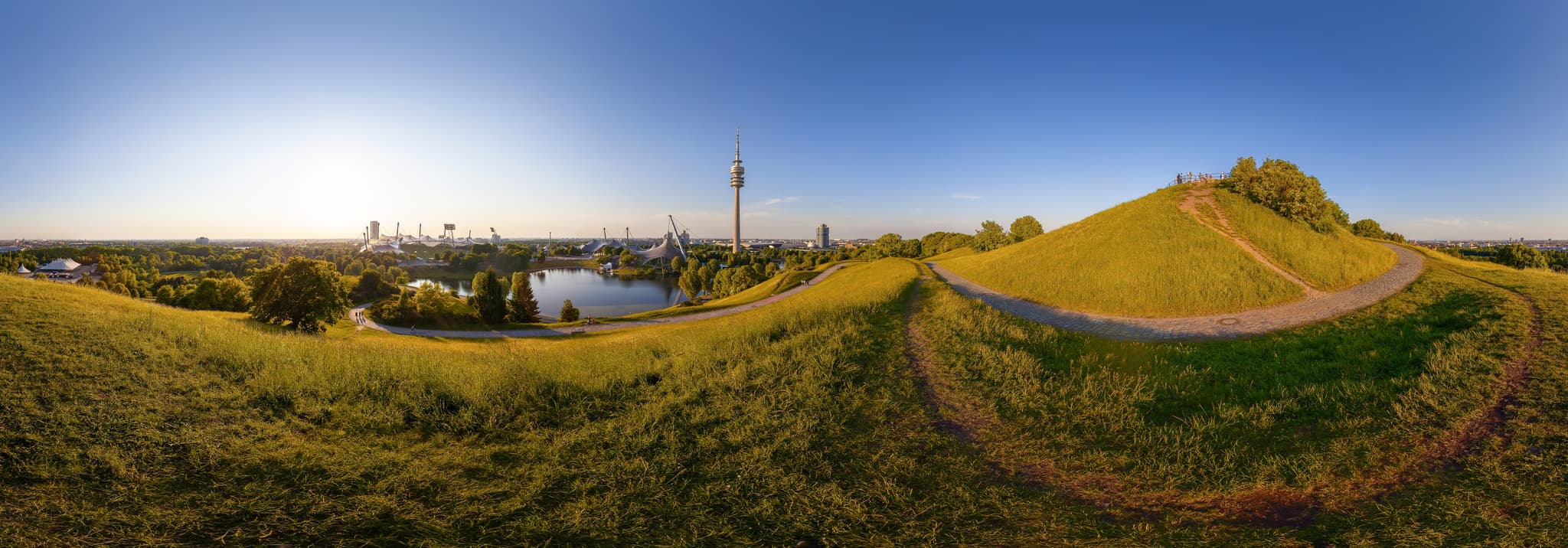 Panoramablick vom Hügel im Olympiapark München, Oberbayern, Deutschland. Die Aufnahme zeigt den Park, See, Fernsehturm und die Stadt im Münchner Umland.