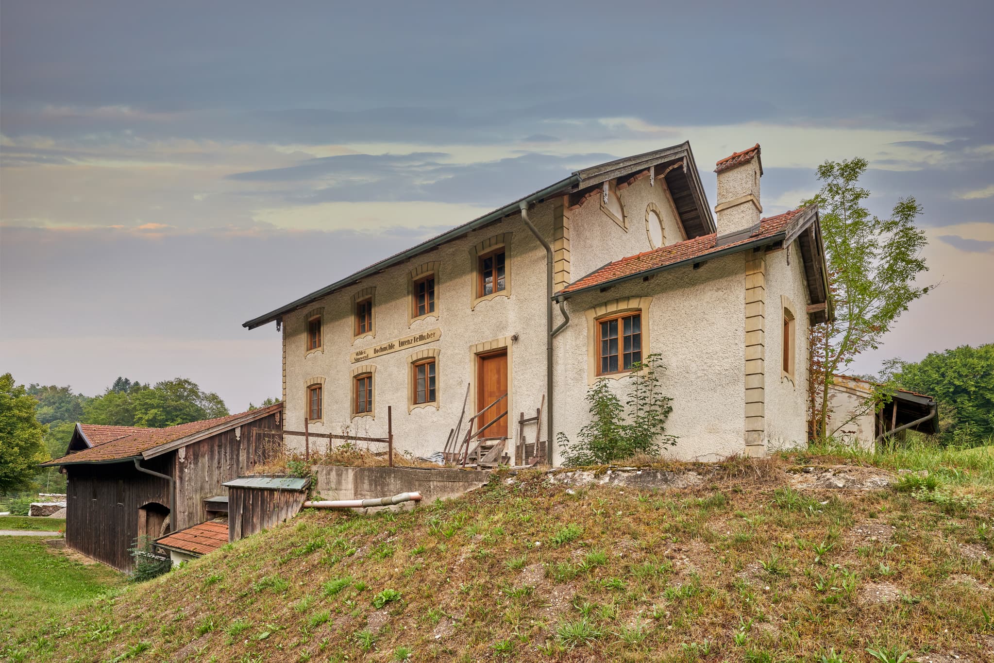 Historische Hochmühle Reischach Bach in Reischach, Altötting, Oberbayern, Inn-Salzach, Deutschland. Altes Gebäude auf einem Grashügel.